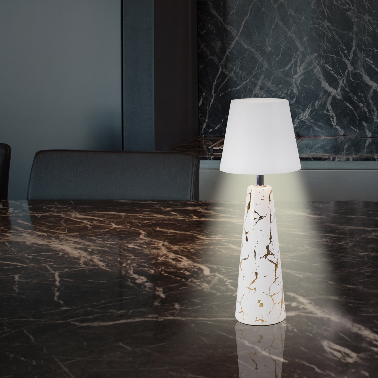 Una lampada bianca con base venata d'oro su tavolo in marmo. Paralume bianco sopra. Sfondo grigio scuro.