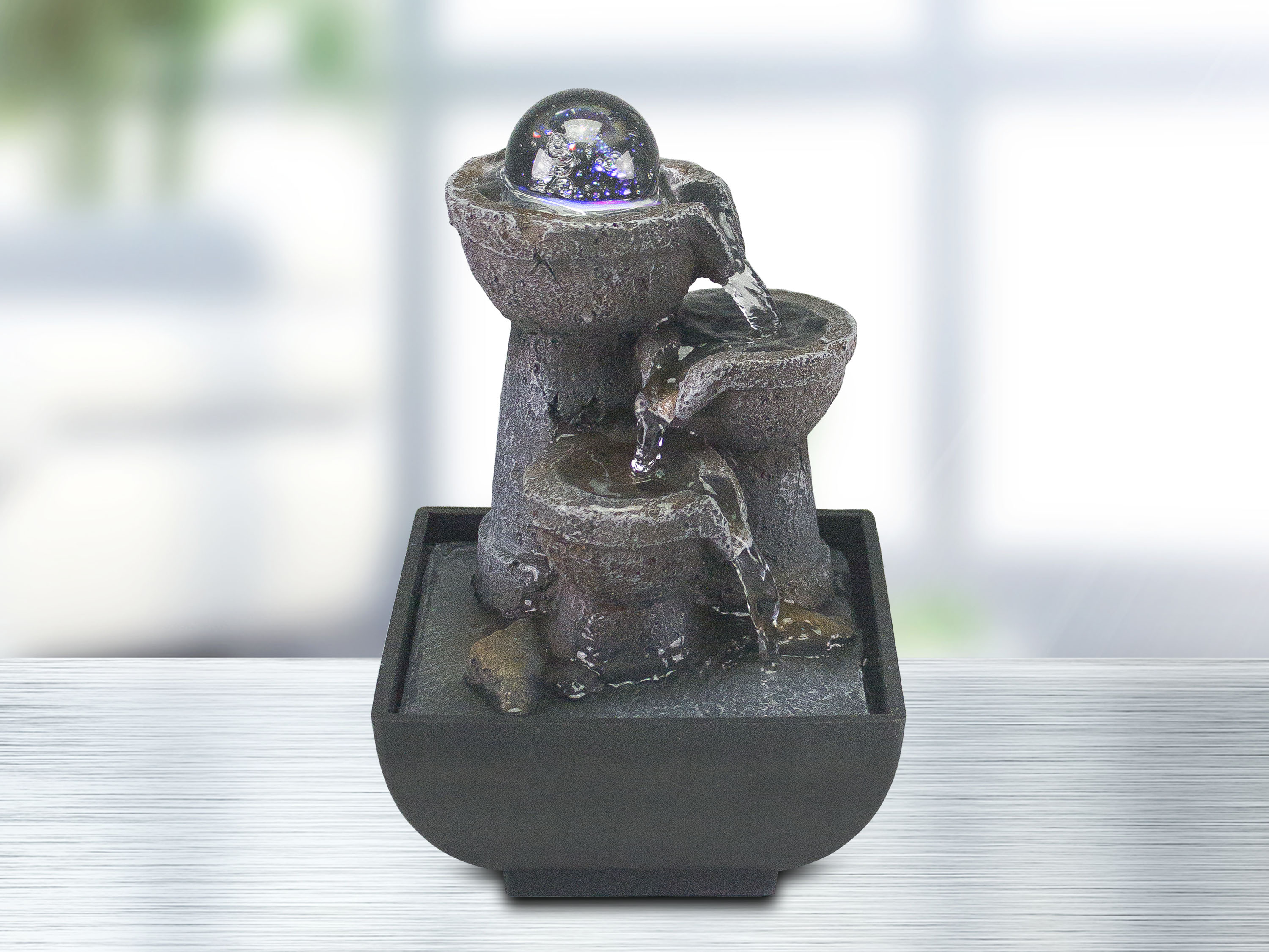 Una fontana decorativa con sfera di vetro. L'acqua scorre a cascata in una base nera.
