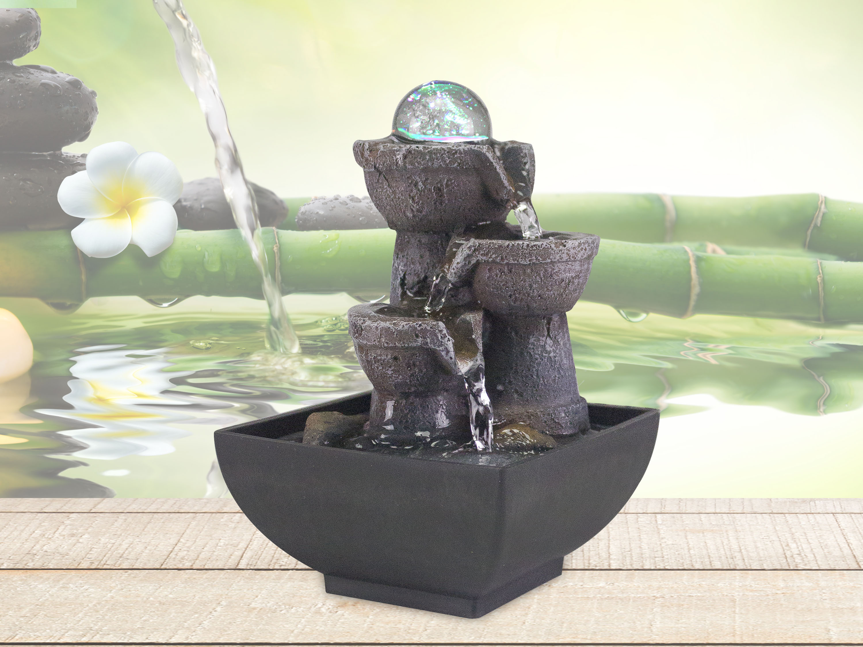 Una fontana decorativa con una sfera di vetro sulla cima. L'acqua scorre lungo i livelli. Bambù e un fiore sullo sfondo.