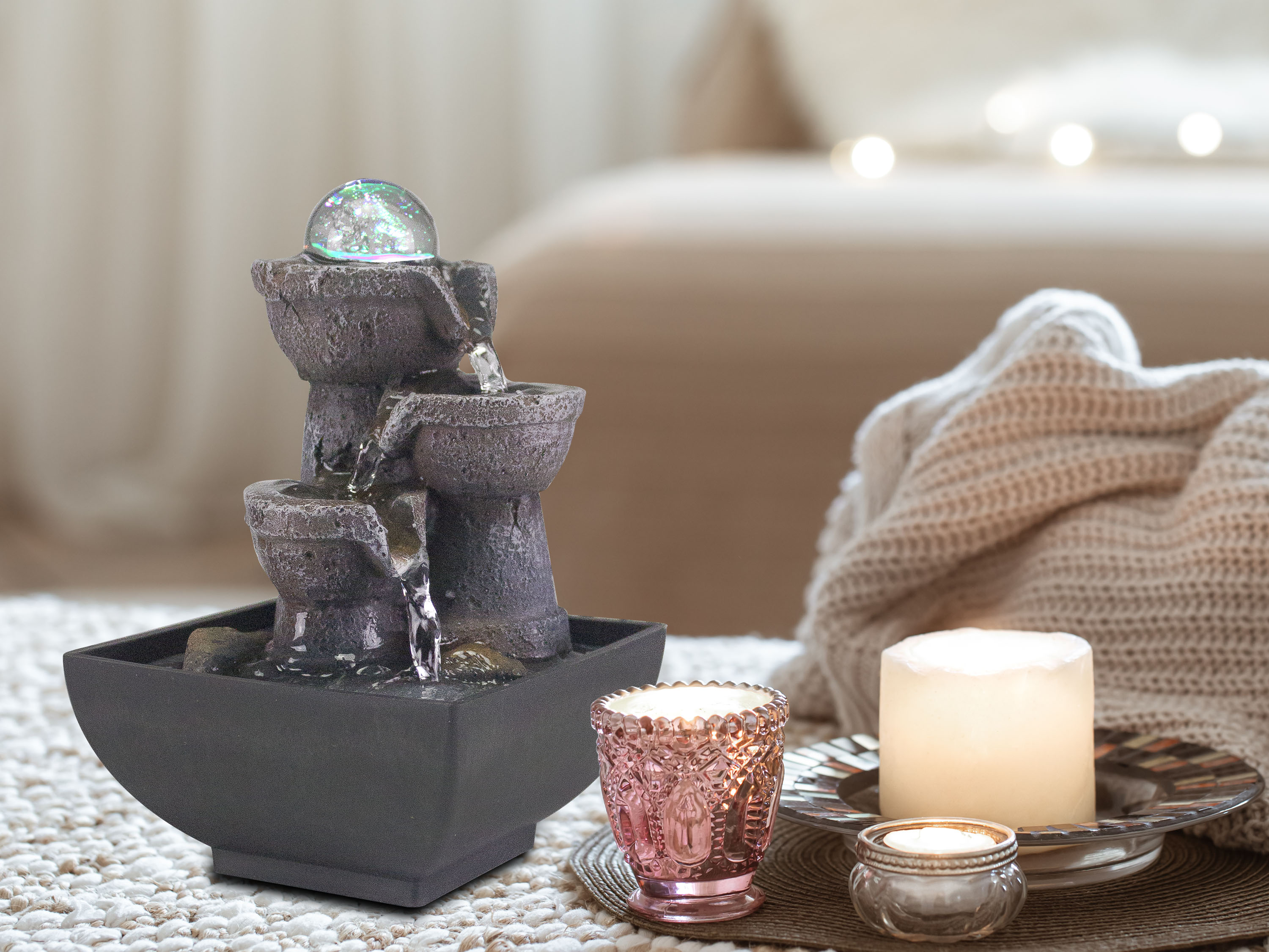 Una fontana decorativa con una palla di vetro, candele e una coperta su un tavolo.