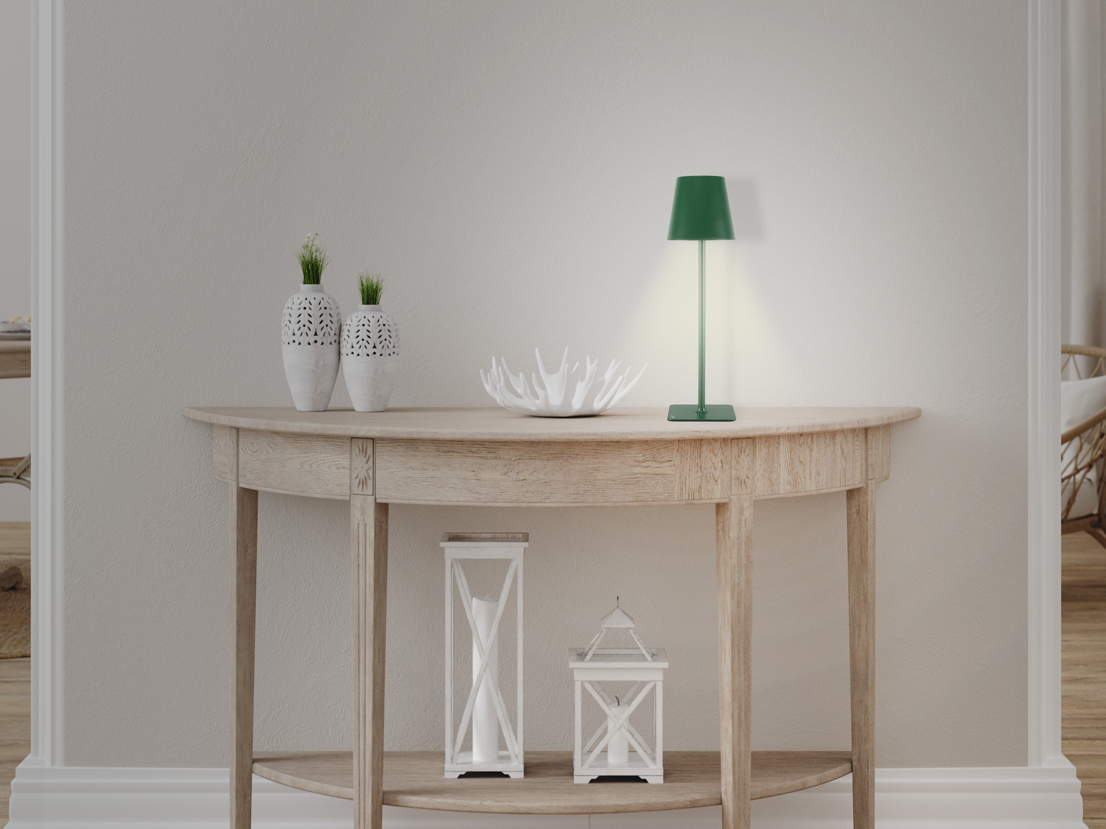 Un tavolo con vasi, lampada e lanterne. Una lampada verde illumina il tavolo. Mobili in legno chiaro, pareti bianche.