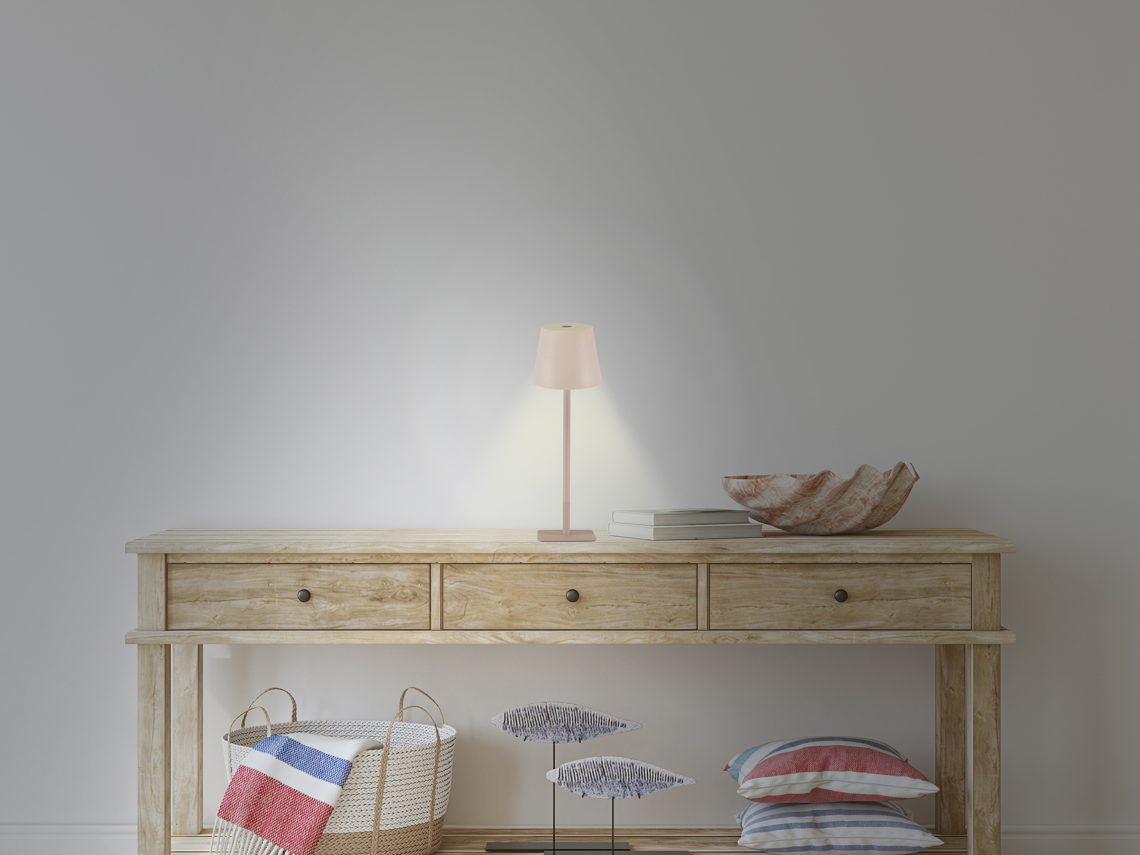 Consolle in legno con lampada, libri, conchiglia, cesto, pesci decorativi e cuscini. Sfondo muro bianco.