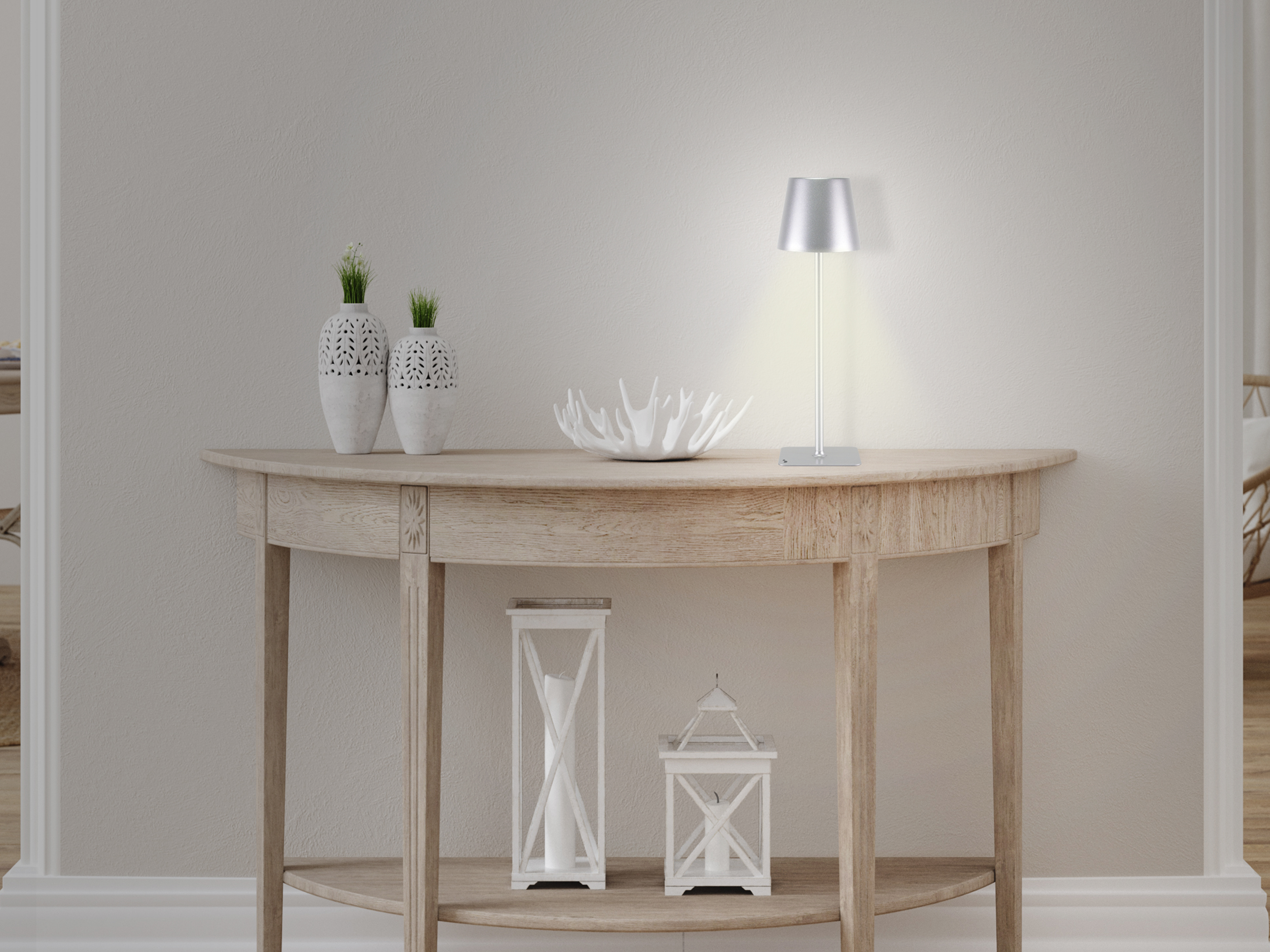 Un tavolo con vasi, lampada e ciotola decorativa. Due lanterne sul ripiano inferiore. Parete e pavimento beige chiaro.