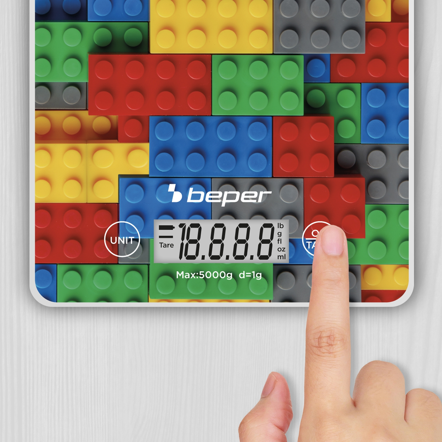 Una mano preme il pulsante 'Tara' su una bilancia. La bilancia ha un design Lego colorato e visualizza '18.8.8.8'.