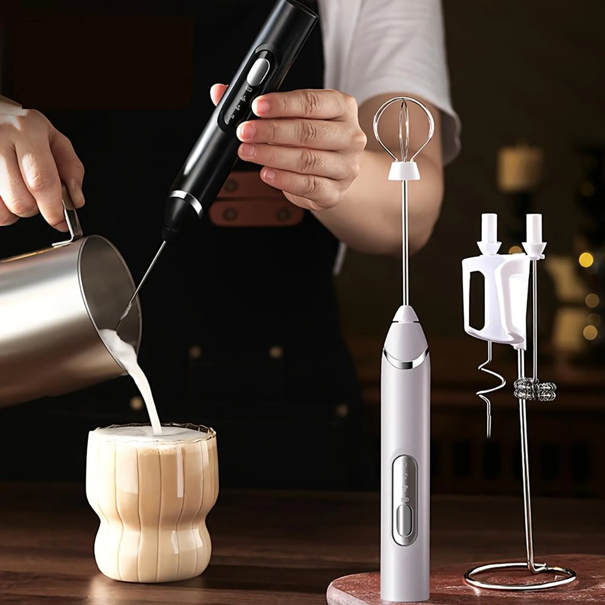Eine Person gießt Milch in ein Glas. Es gibt zwei Milchaufschäumer und einen Ständer. Das Glas ist mit einem Getränk gefüllt.