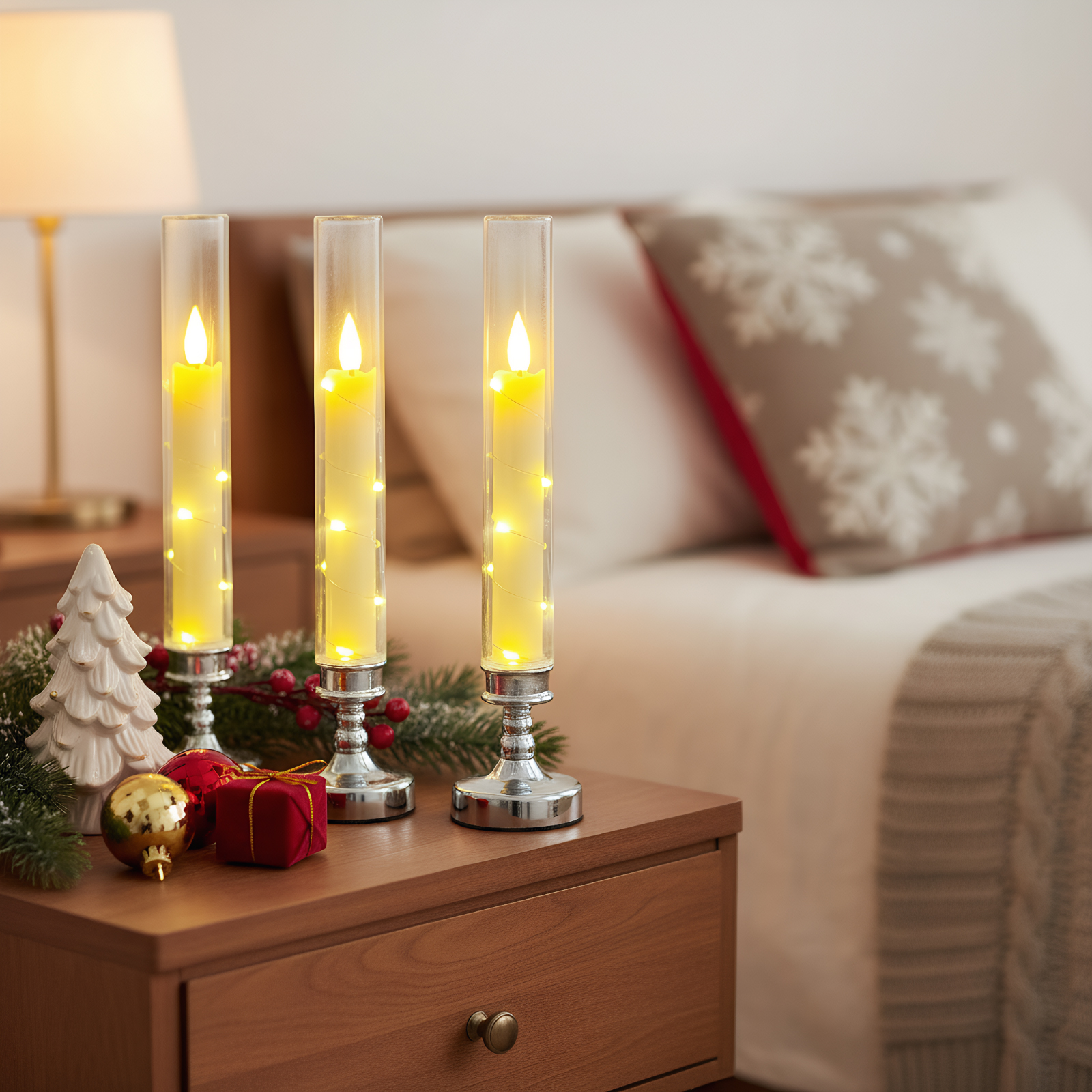 Drei beleuchtete Kerzenhalter auf einem Nachttisch aus Holz mit Weihnachtsdekoration. Im Hintergrund ein Bett.