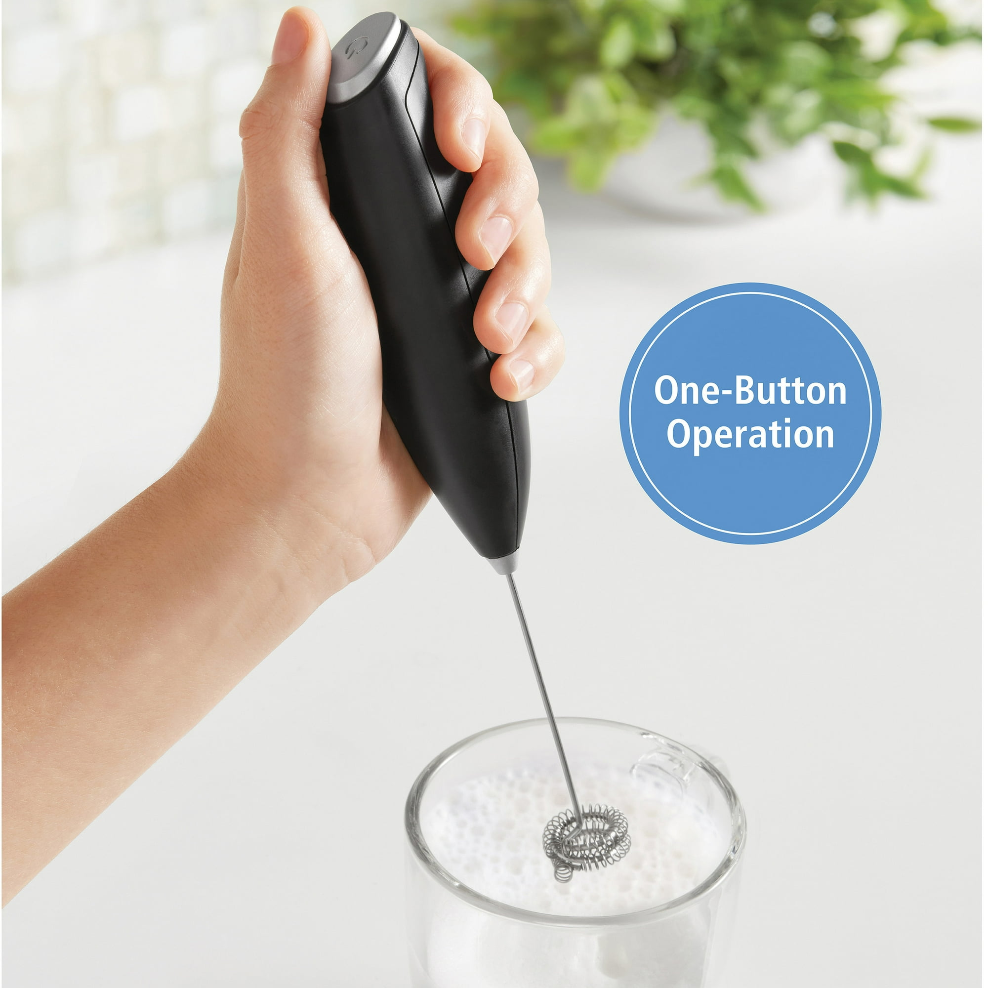 Eine Hand hält einen schwarzen Aufschäumer, der Milch in einem Glas aufschäumt. Ein blauer Kreis sagt 'One-Button Operation'.