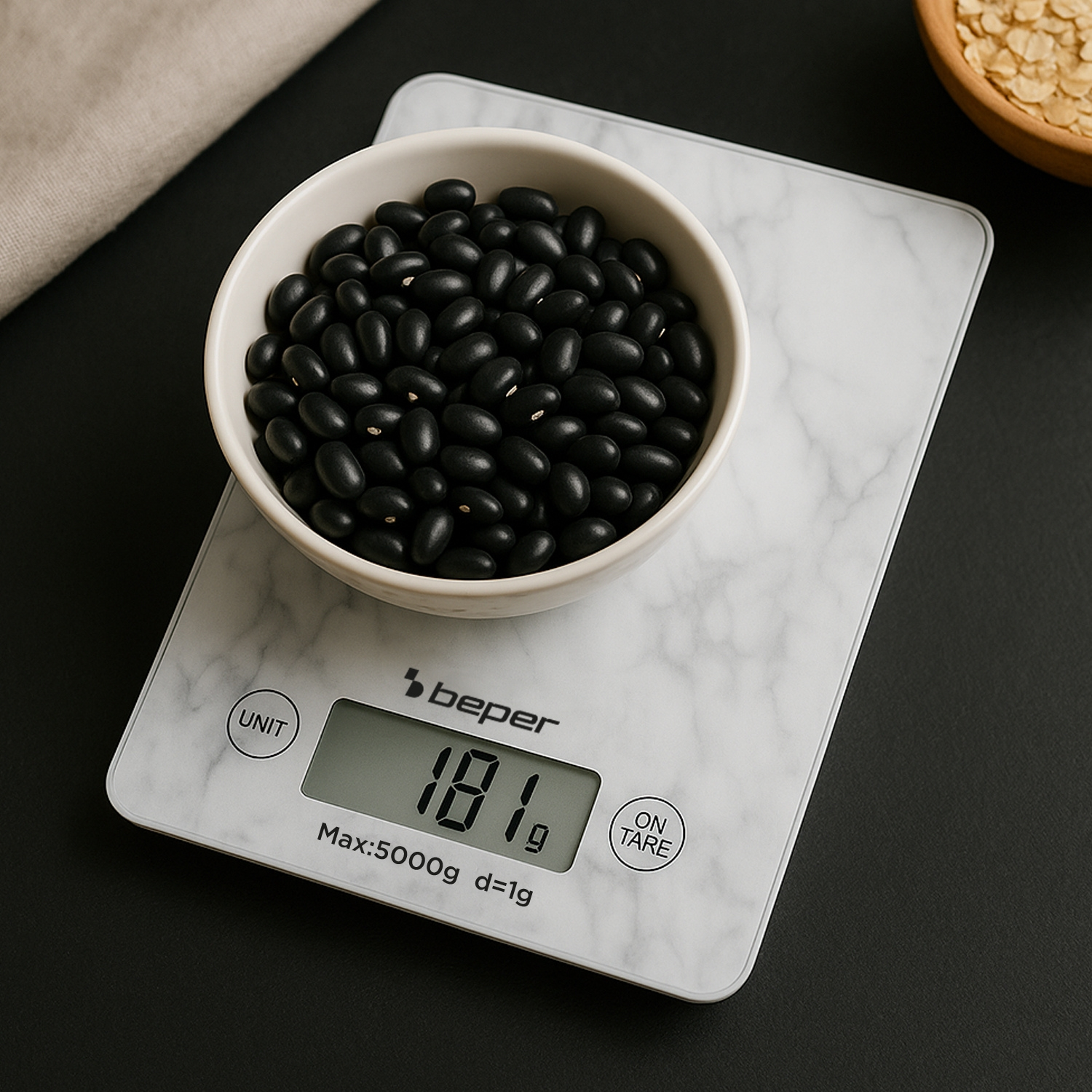 Una ciotola bianca piena di fagioli neri su una bilancia da cucina digitale, che mostra 181 g. La bilancia poggia su una superficie marmorizzata.