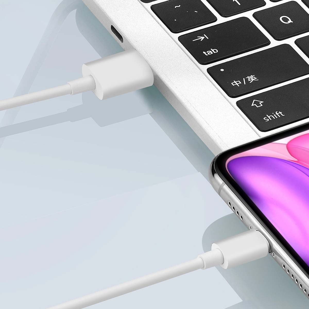 Un câble de charge blanc relie un ordinateur portable et un smartphone. Le clavier de l'ordinateur portable est noir et blanc, le téléphone est argenté.