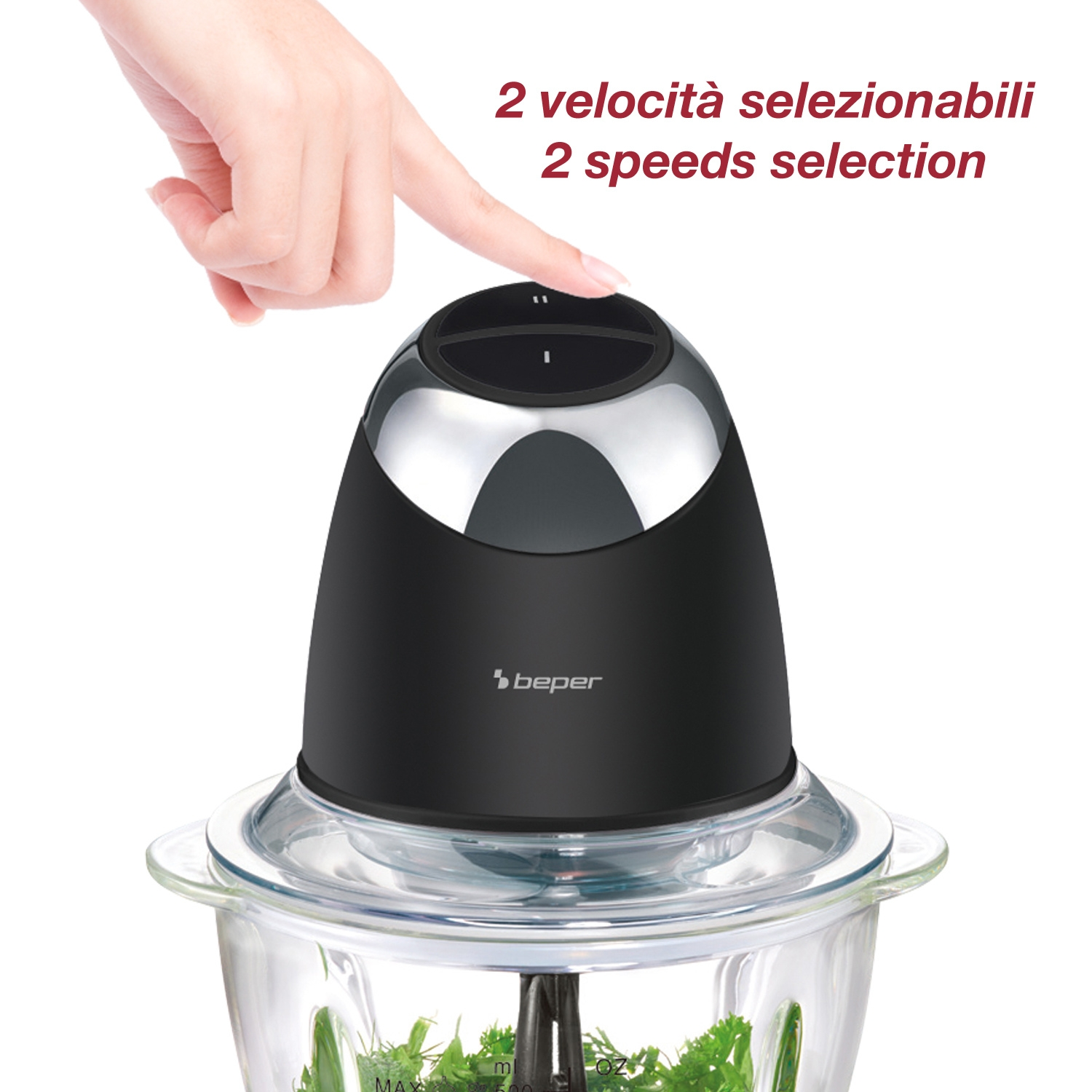 Una mano preme un pulsante su un robot da cucina nero e argento. Il robot ha una ciotola di vetro piena di erbe.