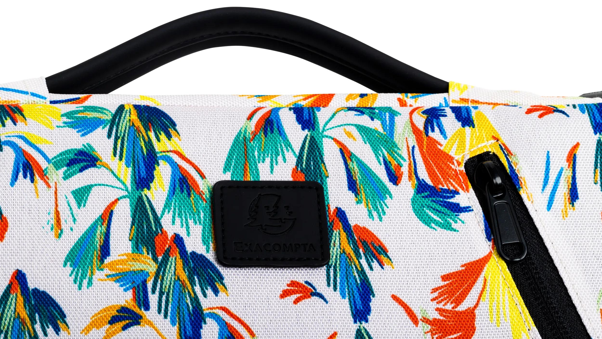 Una borsa fantasia con foglie tropicali colorate. Sono visibili un manico e una cerniera neri. Include una toppa nera del marchio.