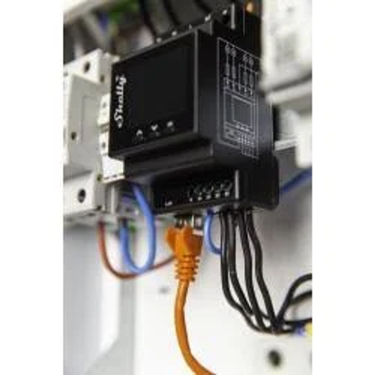 Czarne urządzenie Shelly z przewodami i pomarańczowym kablem Ethernet jest zamontowane w panelu elektrycznym.