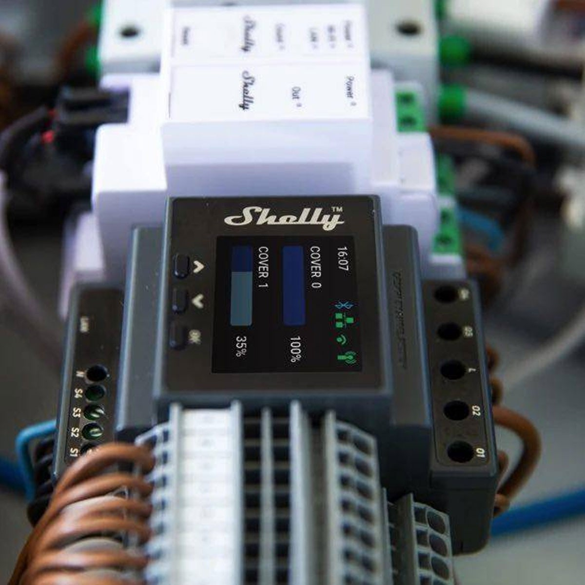 Zbliżenie elementów elektrycznych, w tym urządzenia Shelly z ekranem wyświetlającym dane i dwa procenty pokrycia.