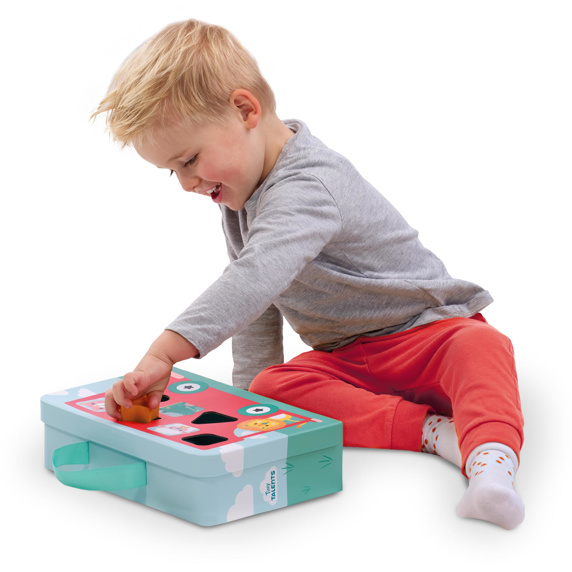 Un niño juega con una caja de juguetes. La caja tiene agujeros y formas. El niño sonríe y mete una forma en un agujero.