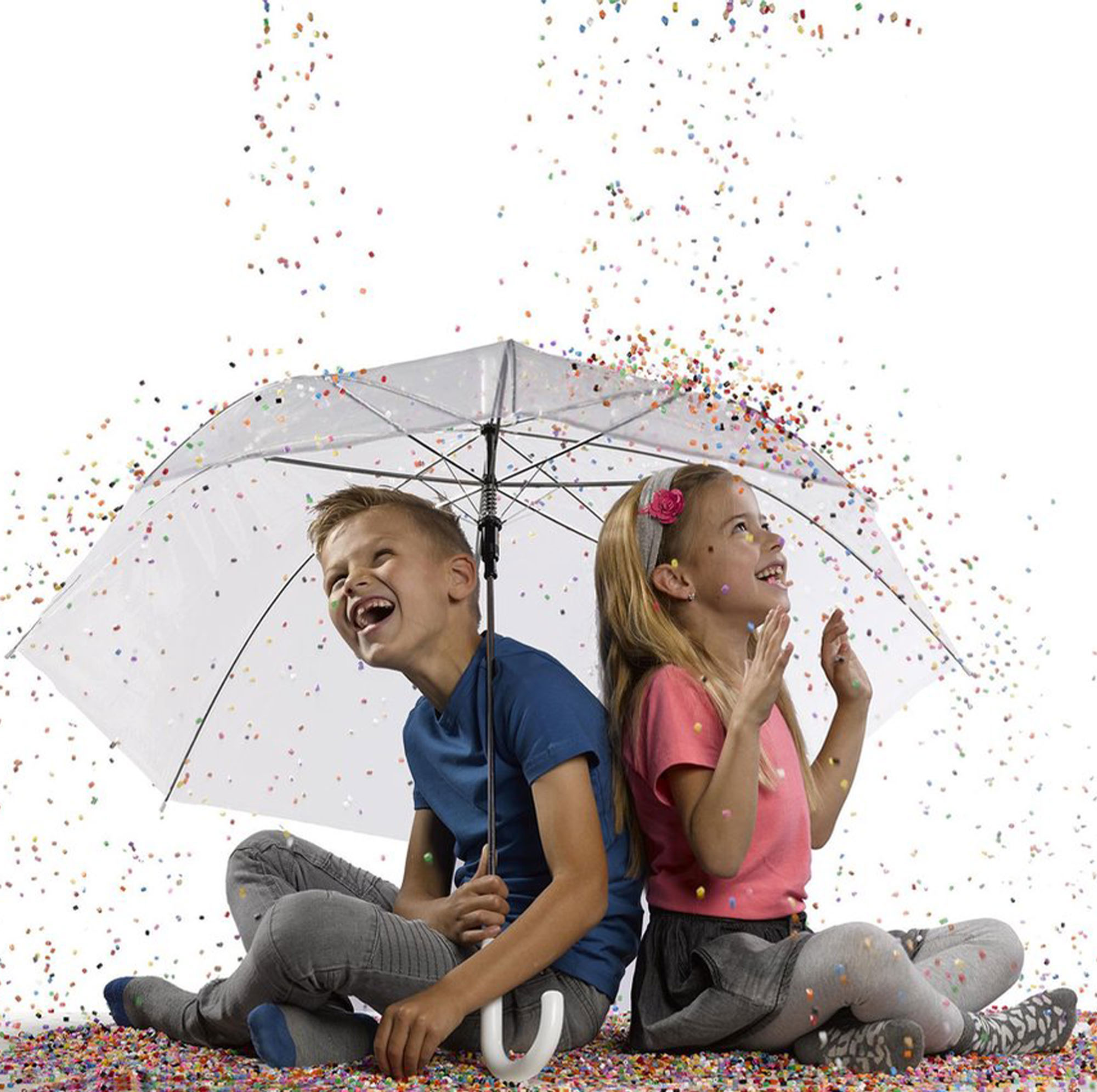 Zwei Kinder sitzen unter einem Regenschirm und lachen, während Konfetti fällt. Der Hintergrund ist weiß.