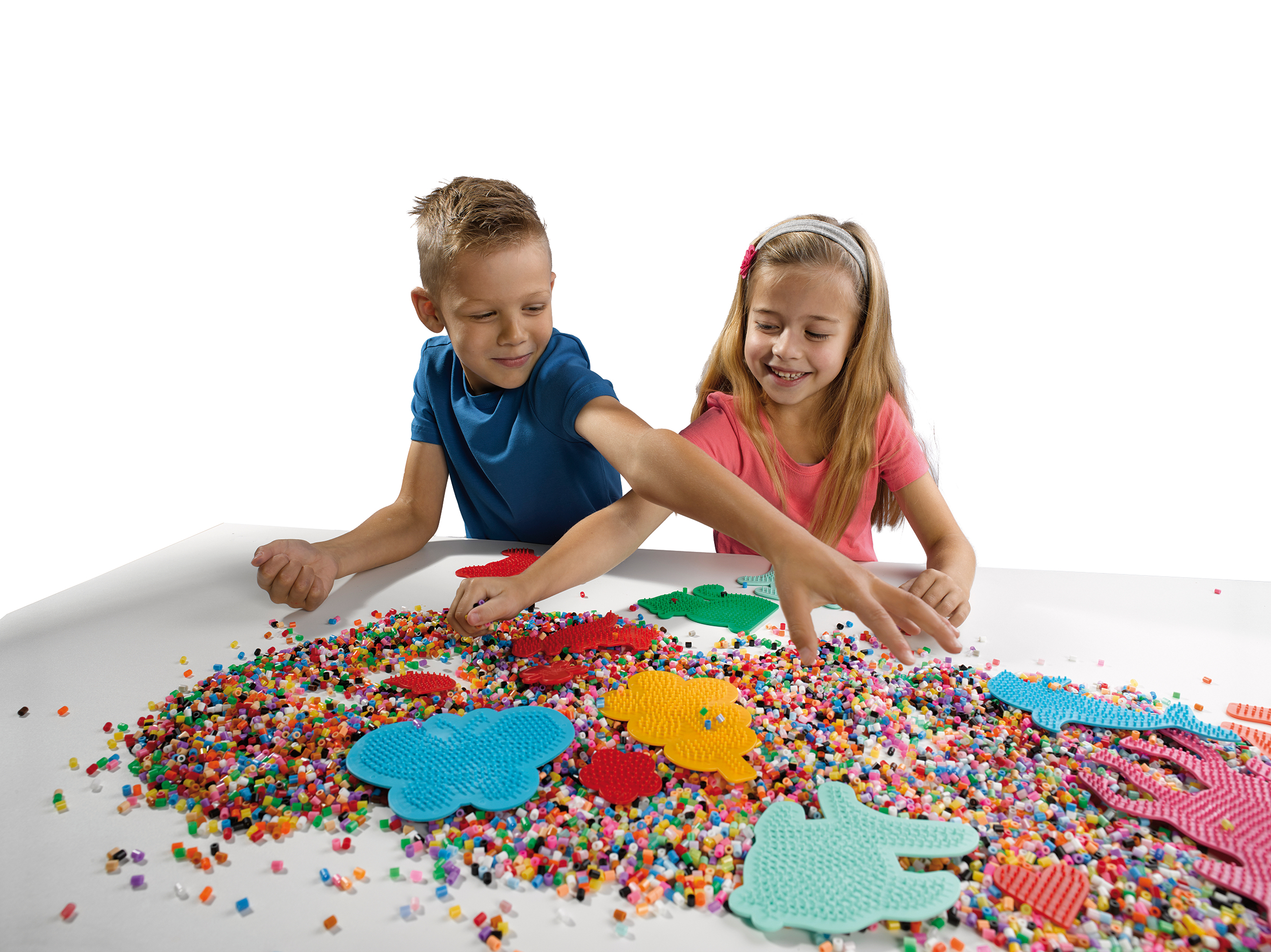 Zwei Kinder spielen mit bunten Perlen auf einem weißen Tisch und legen sie auf geformte Steckbretter.
