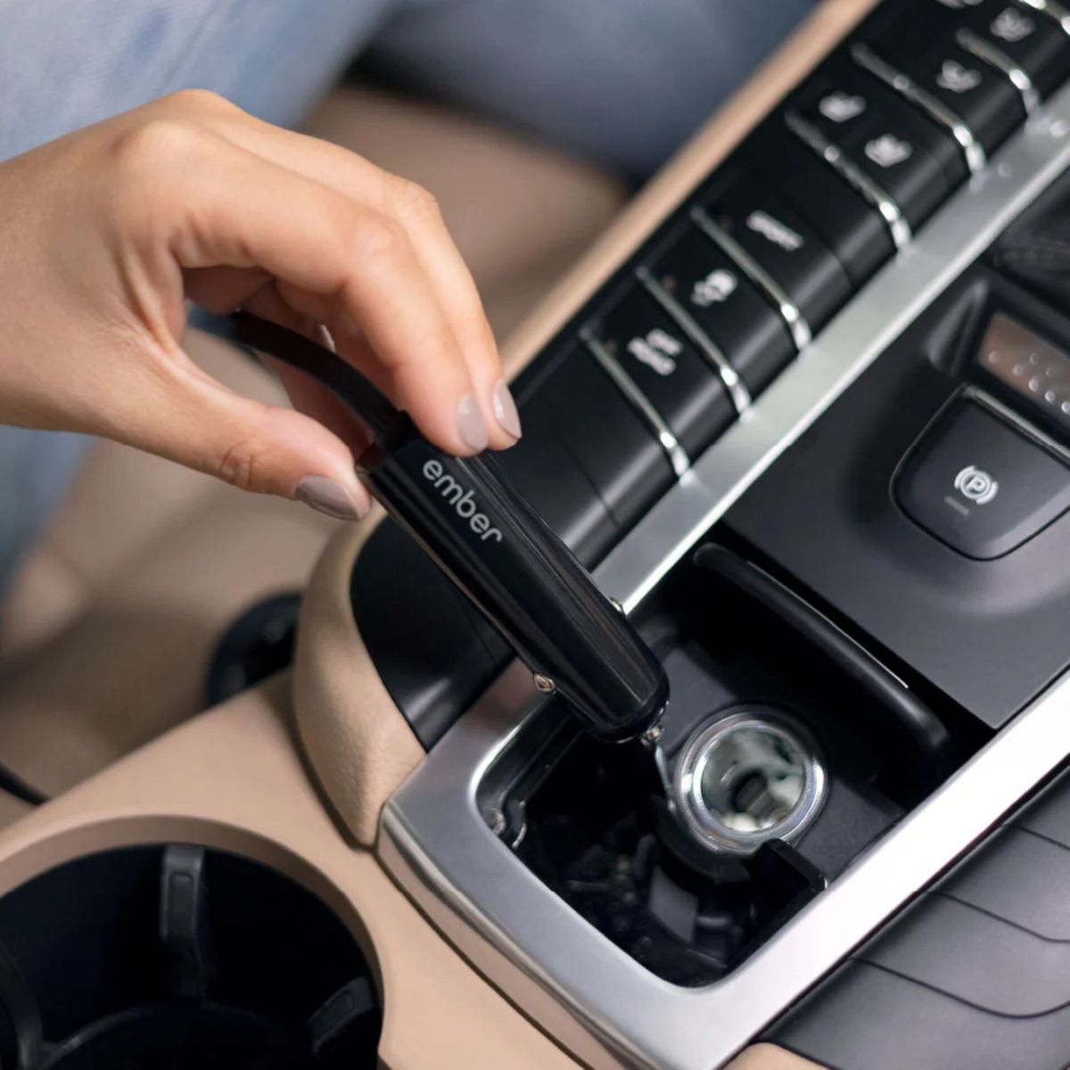 Eine Hand steckt ein schwarzes 'ember'-Gerät in den Zigarettenanzünder eines Autos. Das Auto hat beige und schwarze Paneele.