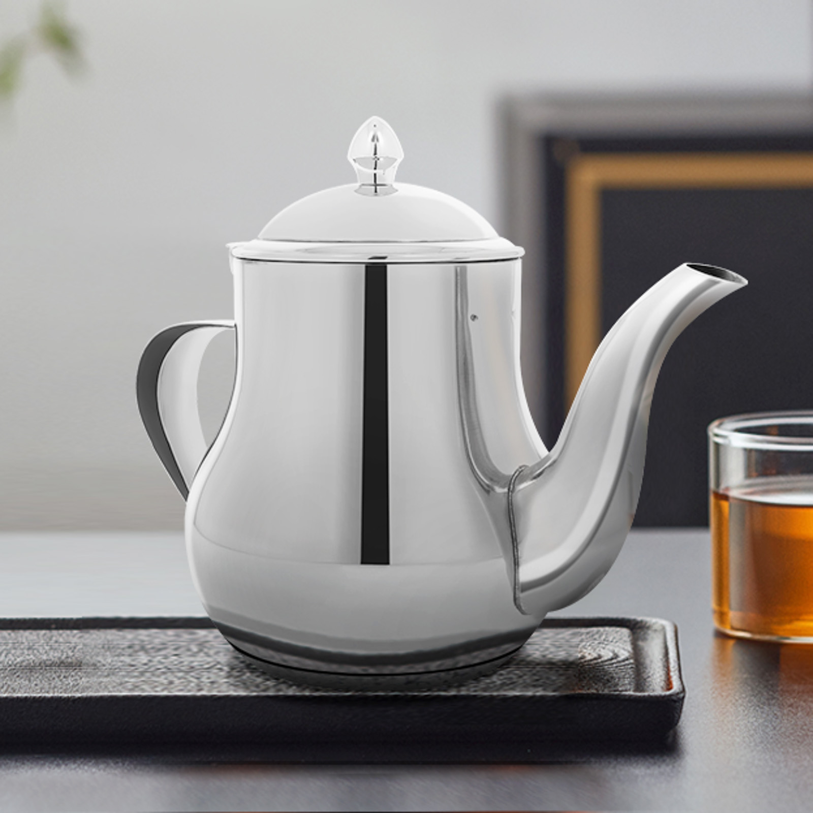 Una tetera plateada brillante con tapa y boquilla, sobre una bandeja. Un vaso de té a la derecha, y un fondo borroso.