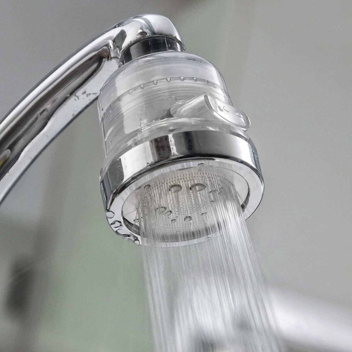 Ein verchromter Wasserhahn mit klarem, fließendem Wasser. Der Wasserhahnhals ist aus klarem Kunststoff und Chrom. Der Hintergrund ist eine verschwommene Wand.