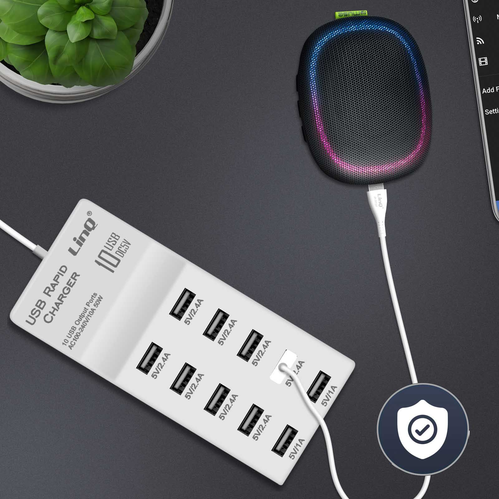 Un caricatore USB bianco con 10 porte, un altoparlante e una pianta su una scrivania. L'altoparlante è collegato al caricatore.