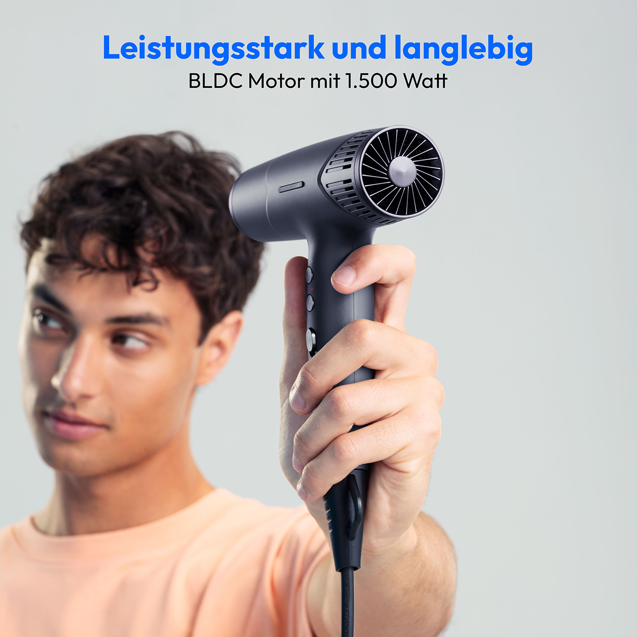 Mężczyzna trzyma czarną suszarkę do włosów. Tekst powyżej mówi 'Mocny i trwały'. Mężczyzna ma na sobie pomarańczową koszulę.