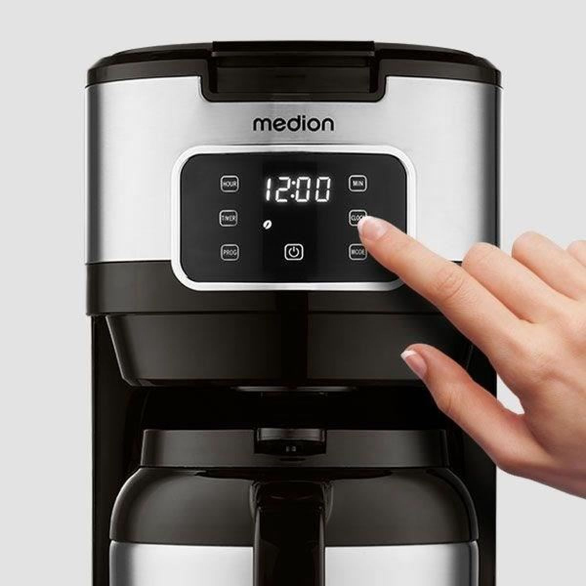 Una mano preme un pulsante su una macchina da caffè. Il display mostra le 12:00. La macchina da caffè è nera e argento.