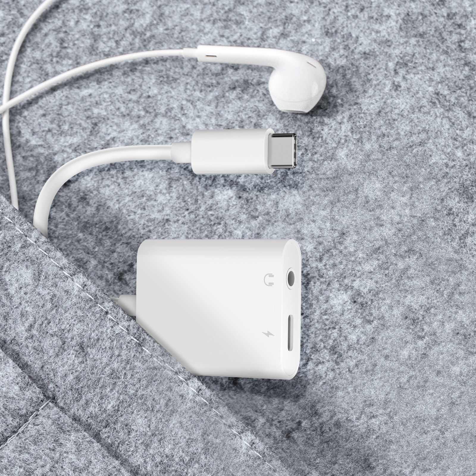 Auricolari, adattatore e cavo bianchi su feltro grigio. L'adattatore ha porte e un fulmine.