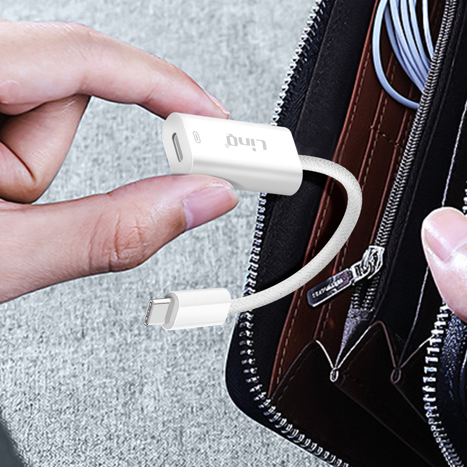 Une main tenant un câble adaptateur blanc avec connecteur USB-C. Un portefeuille noir en arrière-plan.