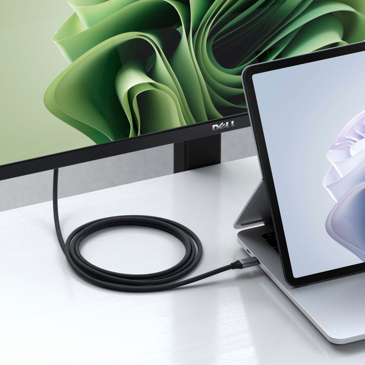 Ein Laptop ist über ein schwarzes Kabel mit einem Monitor verbunden. Der Monitor zeigt grüne, abstrakte Formen und der Laptop einen hellen Hintergrund.