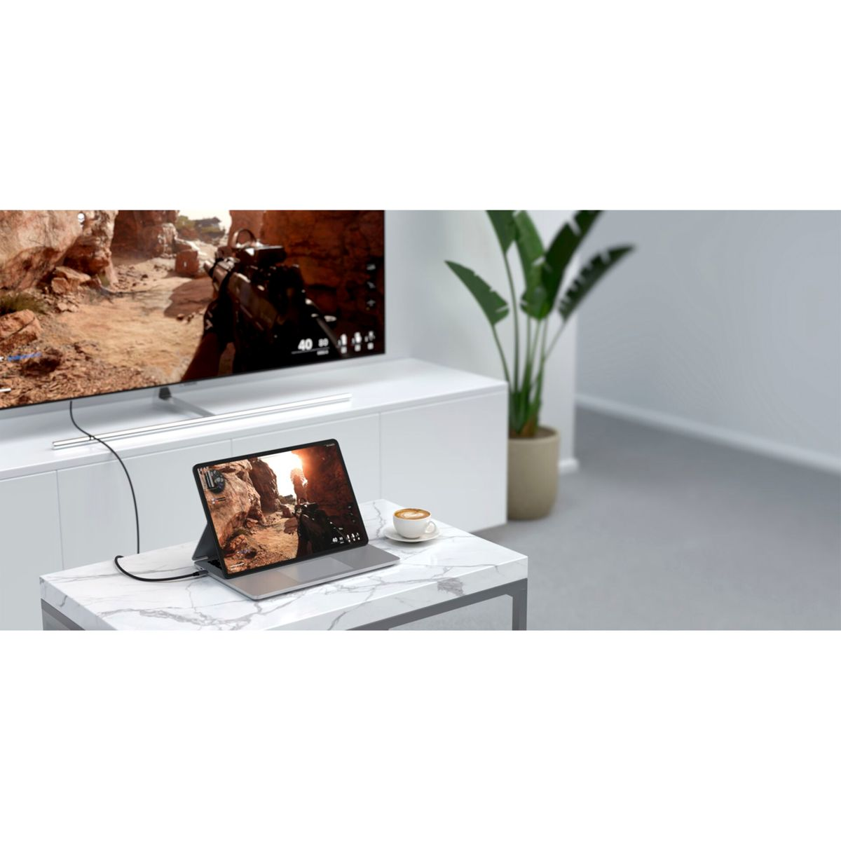 Ein Tablet, das mit einem Fernseher verbunden ist, zeigt ein Videospiel. Auf einem Marmortisch steht eine Tasse Kaffee. Pflanze im Hintergrund.