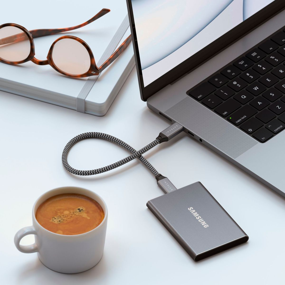 Laptop podłączony do zewnętrznego dysku twardego Samsung. Filiżanka kawy i okulary na stole.