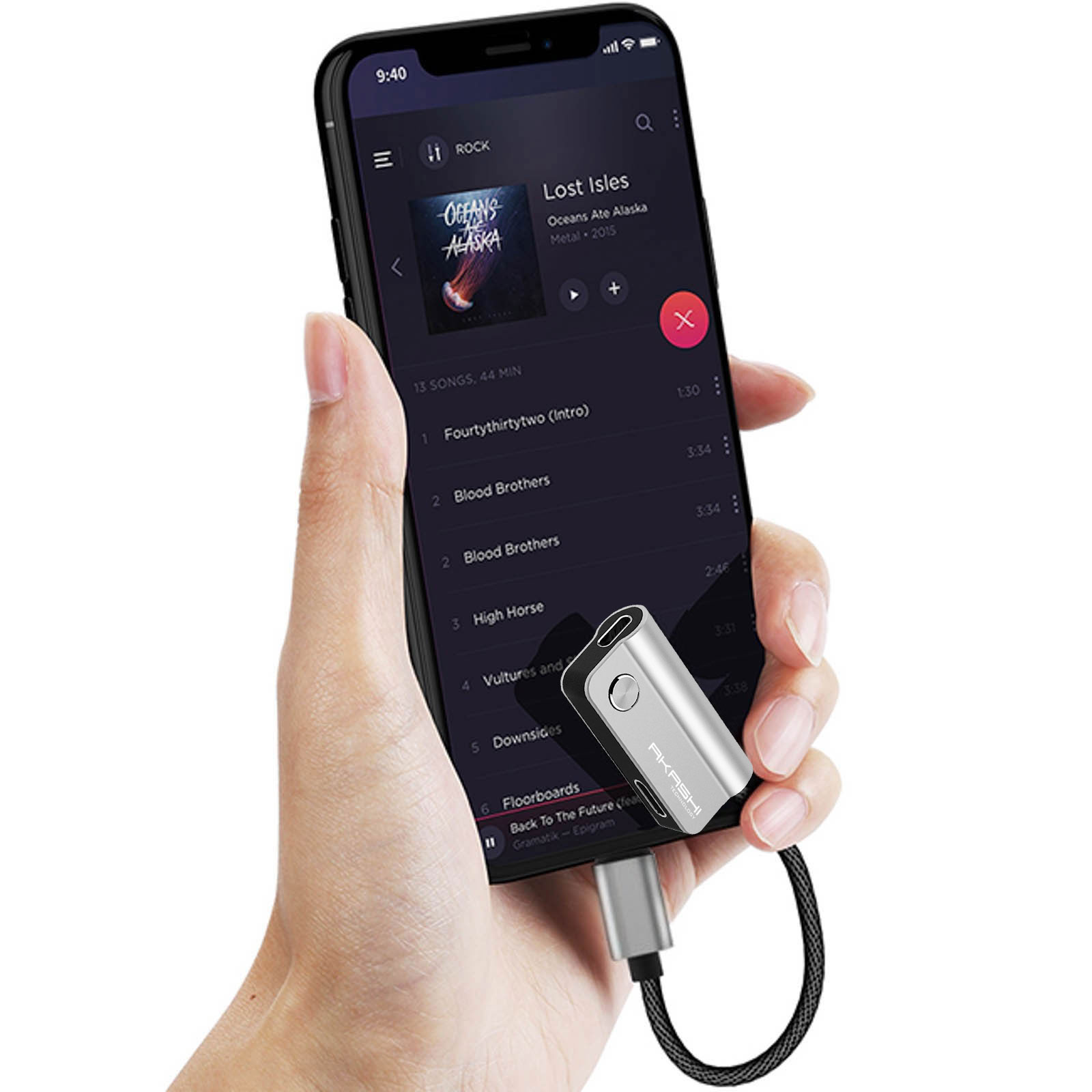 Main tenant un téléphone avec de la musique, connecté à un adaptateur argenté avec un câble noir. Le téléphone affiche les détails de la chanson.