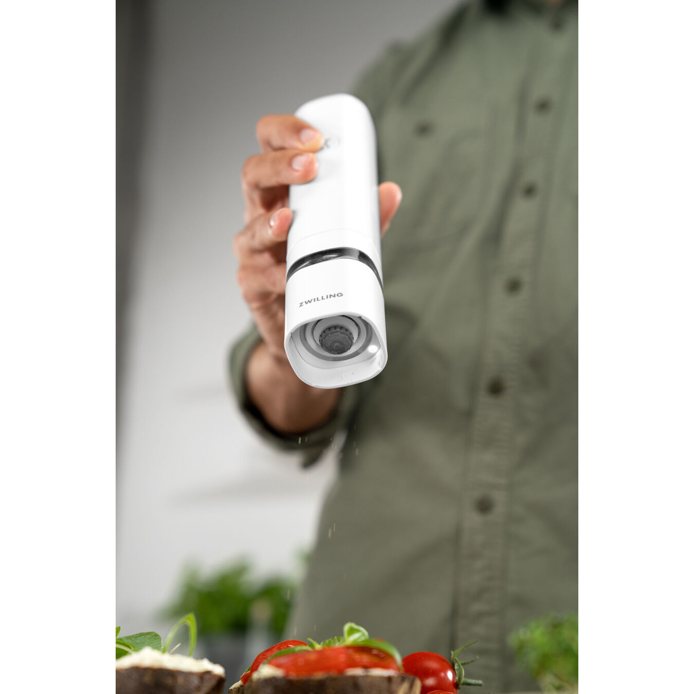 Una persona usa un molinillo de pimienta eléctrico blanco ZWILLING sobre comida. La pimienta cae sobre una tostada con tomate.