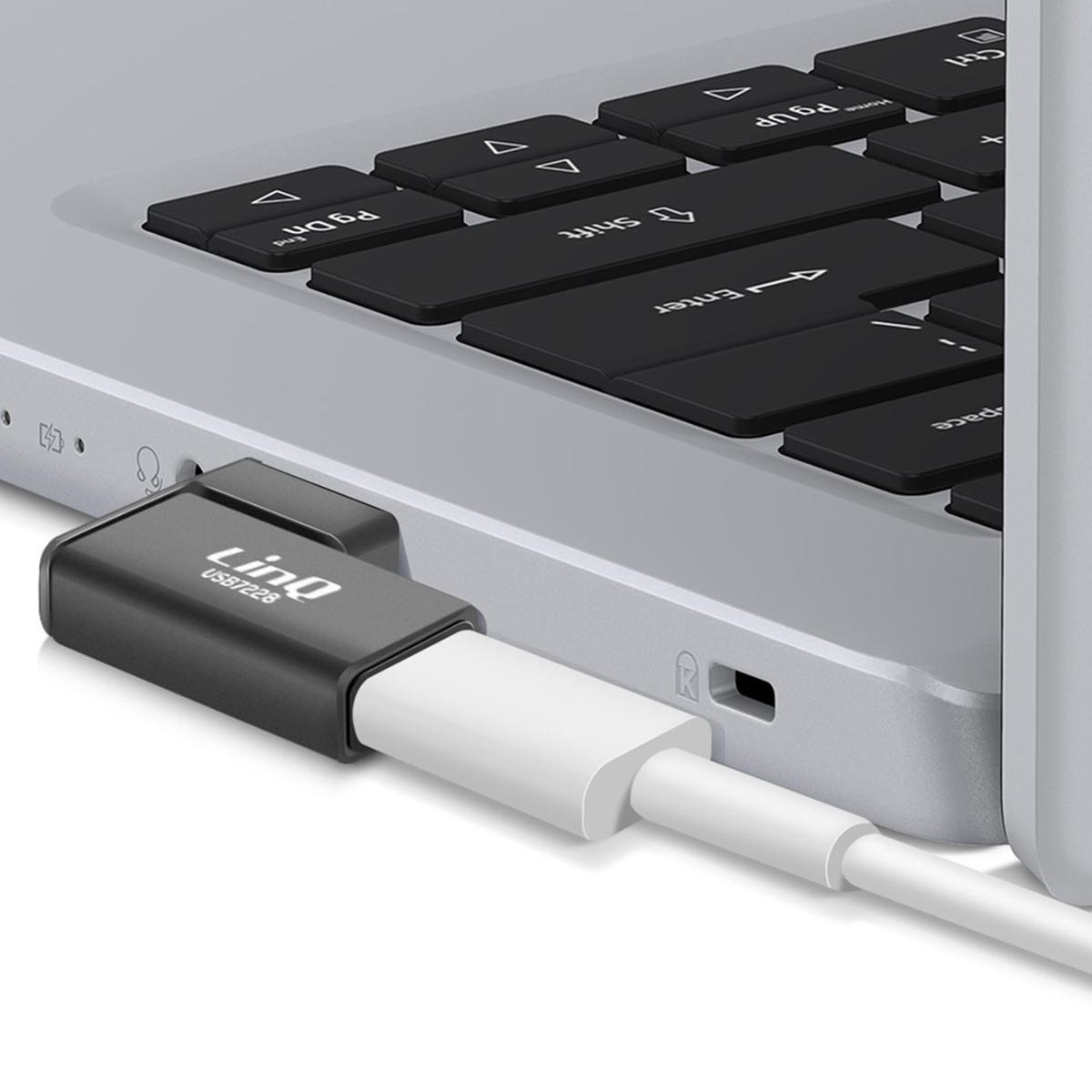 Un adattatore USB-C nero collegato a un laptop. Cavo bianco collegato. Tasti del laptop visibili. L'adattatore ha 'LinQ USB7228' scritto.