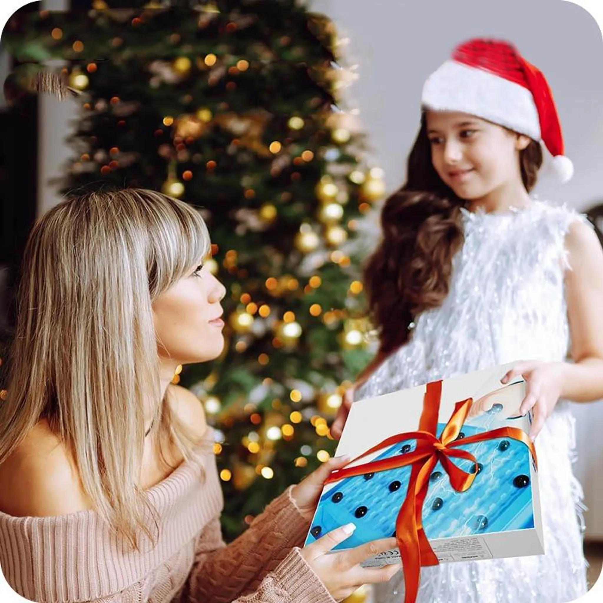 Eine Frau gibt einem Mädchen mit Weihnachtsmütze ein Geschenk. Im Hintergrund ist ein Weihnachtsbaum.