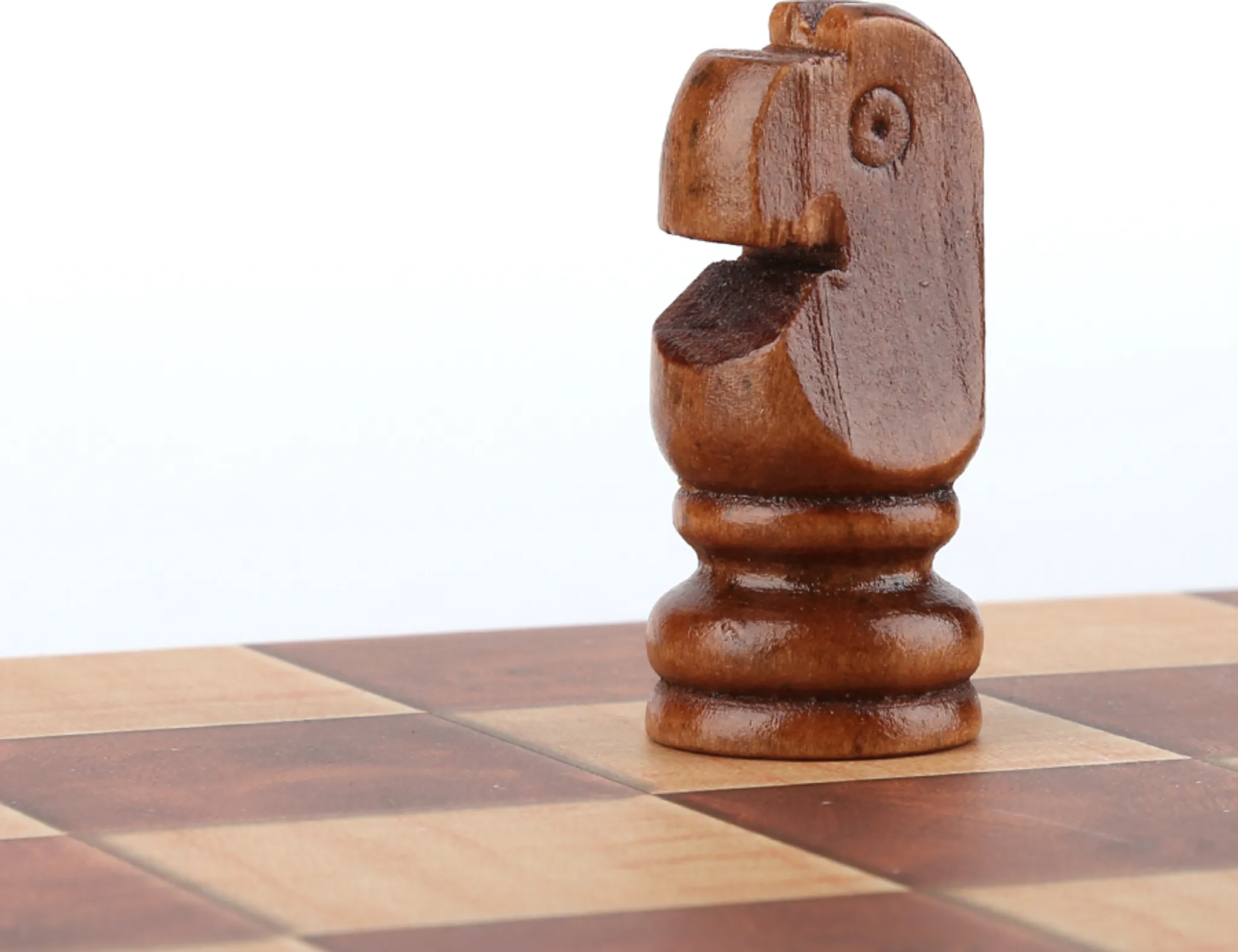 Eine braune hölzerne Springer-Schachfigur auf einem Schachbrett. Der Hintergrund ist weiß.