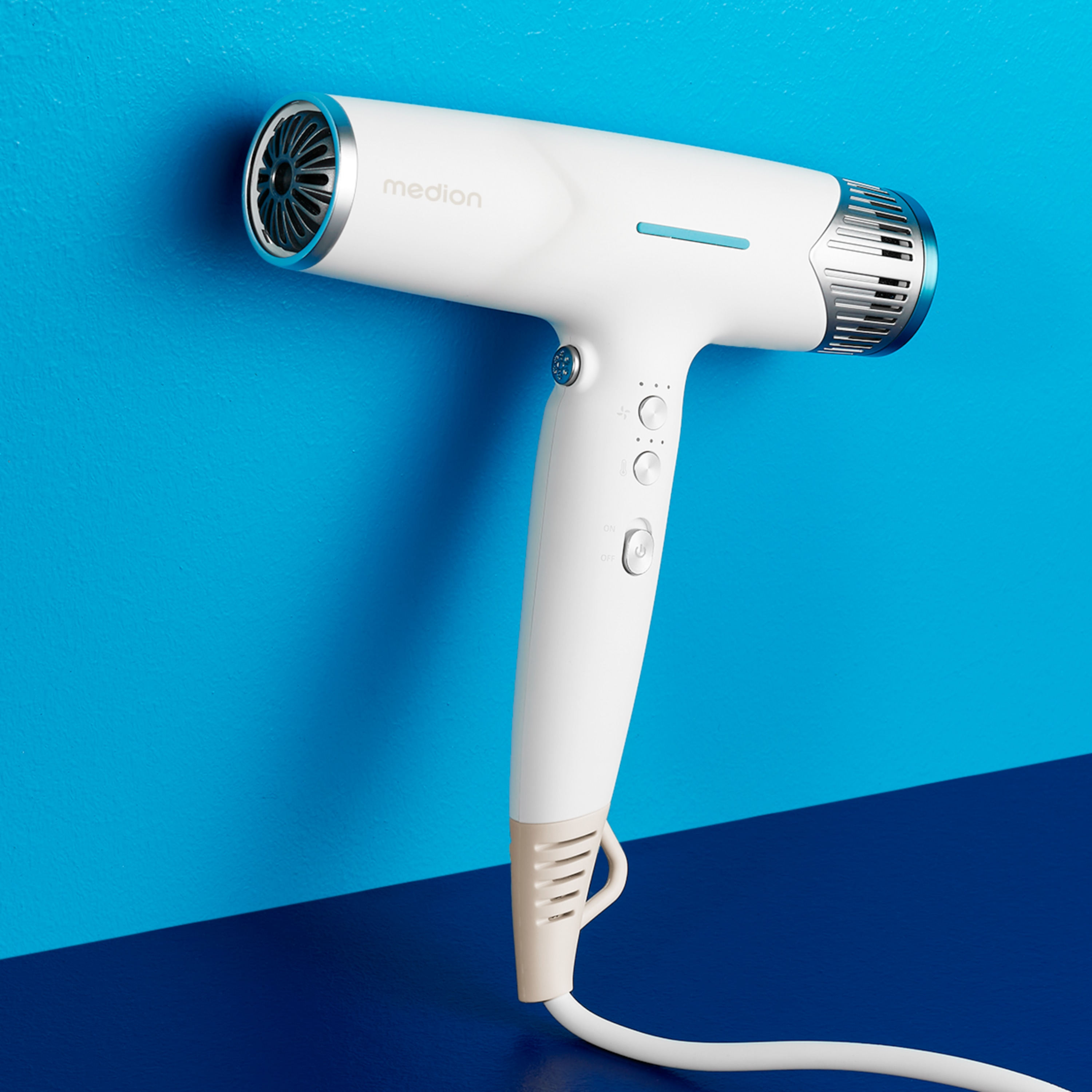 Biała suszarka do włosów Medion na niebieskim tle. Posiada przyciski, wlot powietrza i kabel.