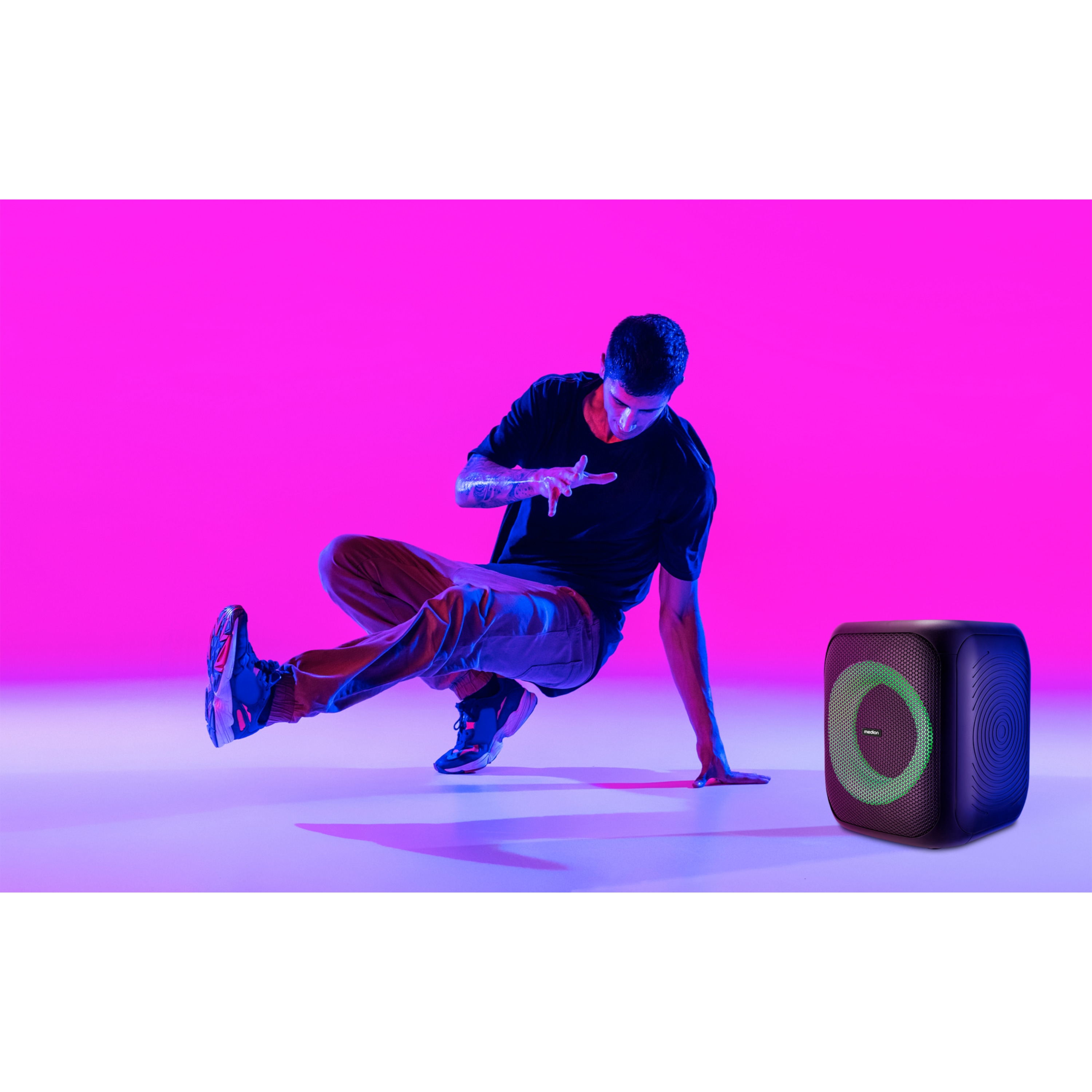Een man die breakdance doet in de buurt van een luidspreker. De achtergrond is roze en de luidspreker is zwart.
