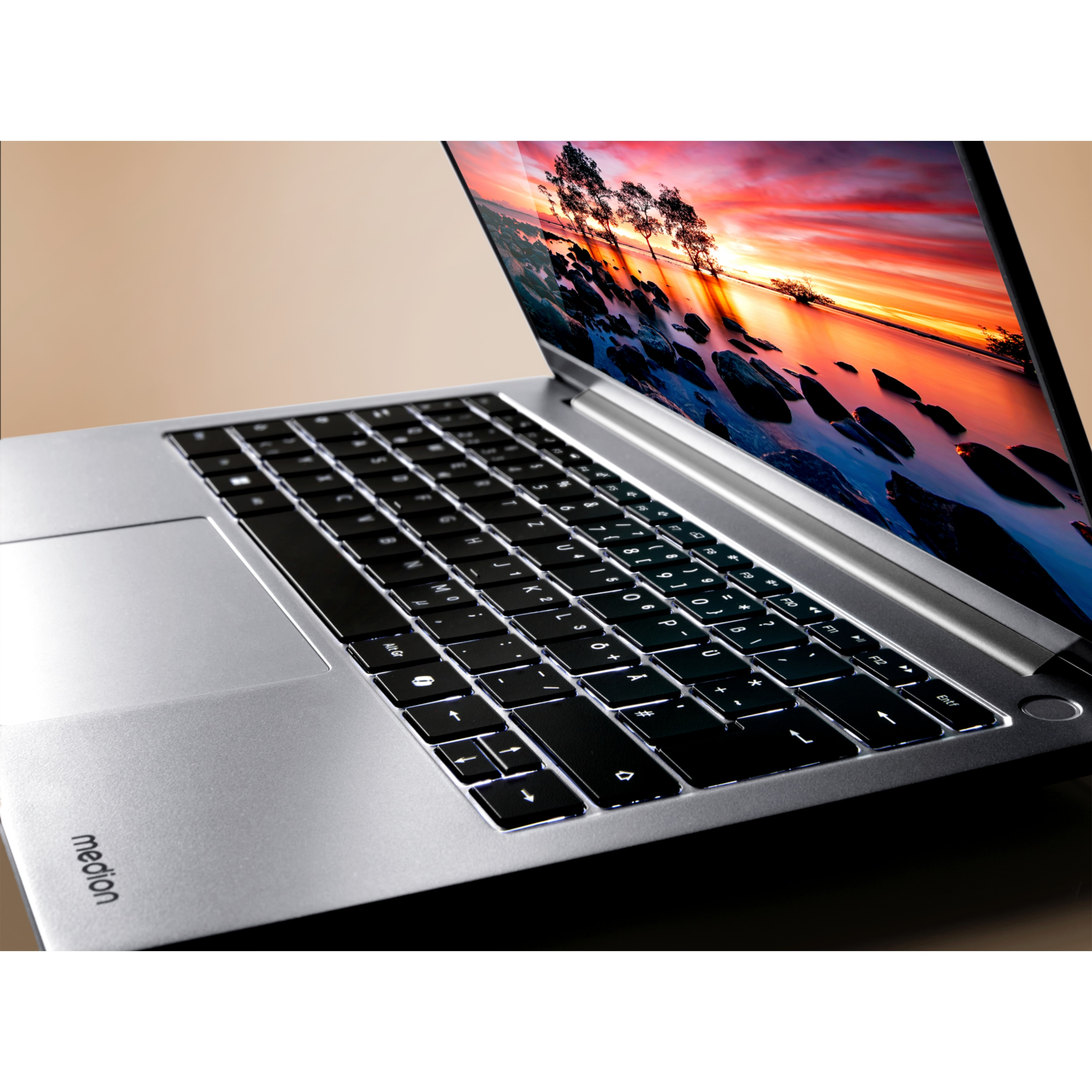Ordinateur portable avec clavier éclairé, écran montrant un coucher de soleil. L'ordinateur est argenté, marque Medion.