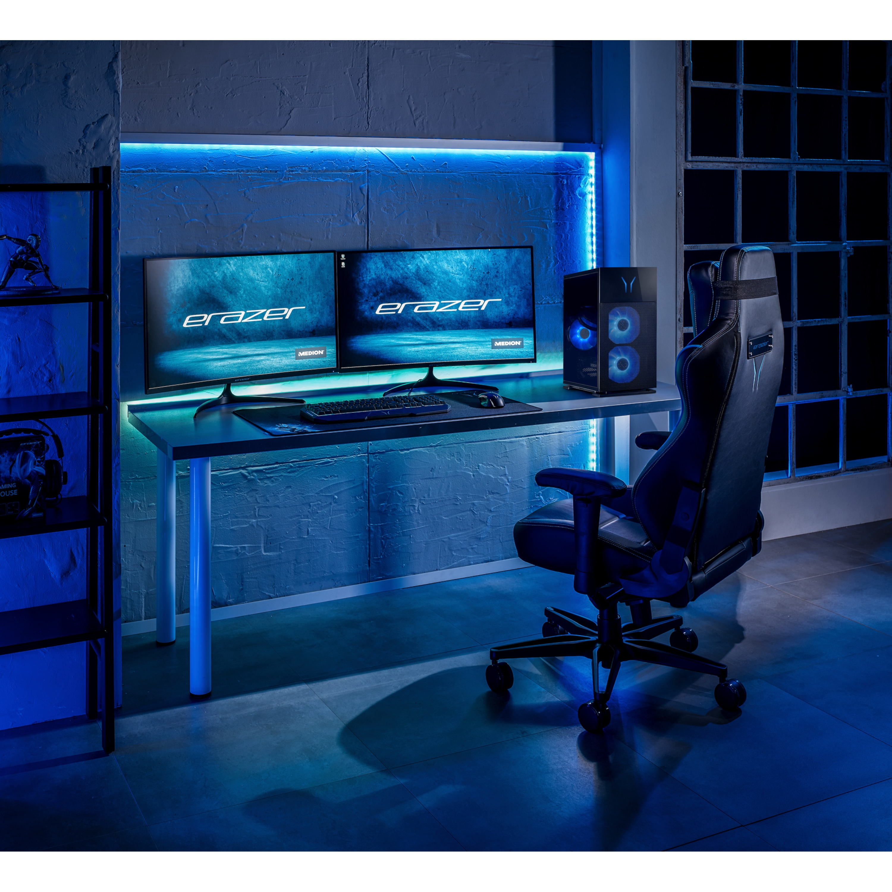 Configurazione di gioco con due monitor, sedia e PC. Illuminazione blu. I monitor mostrano 'eRazer'. Scaffale con statuina a sinistra.