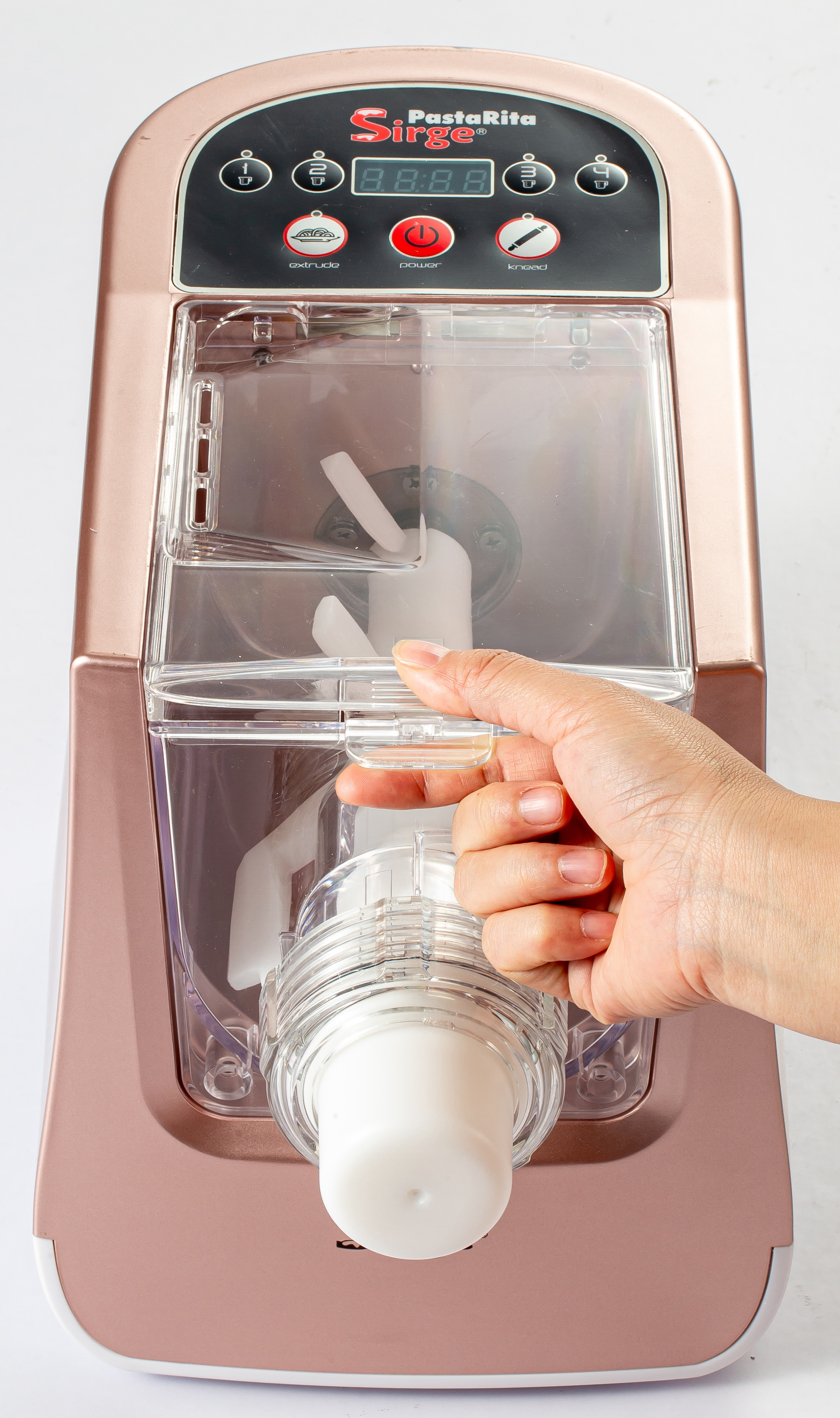 Una mano aziona una macchina per la pasta color oro rosa. La macchina ha un contenitore trasparente, una base bianca e un display digitale.