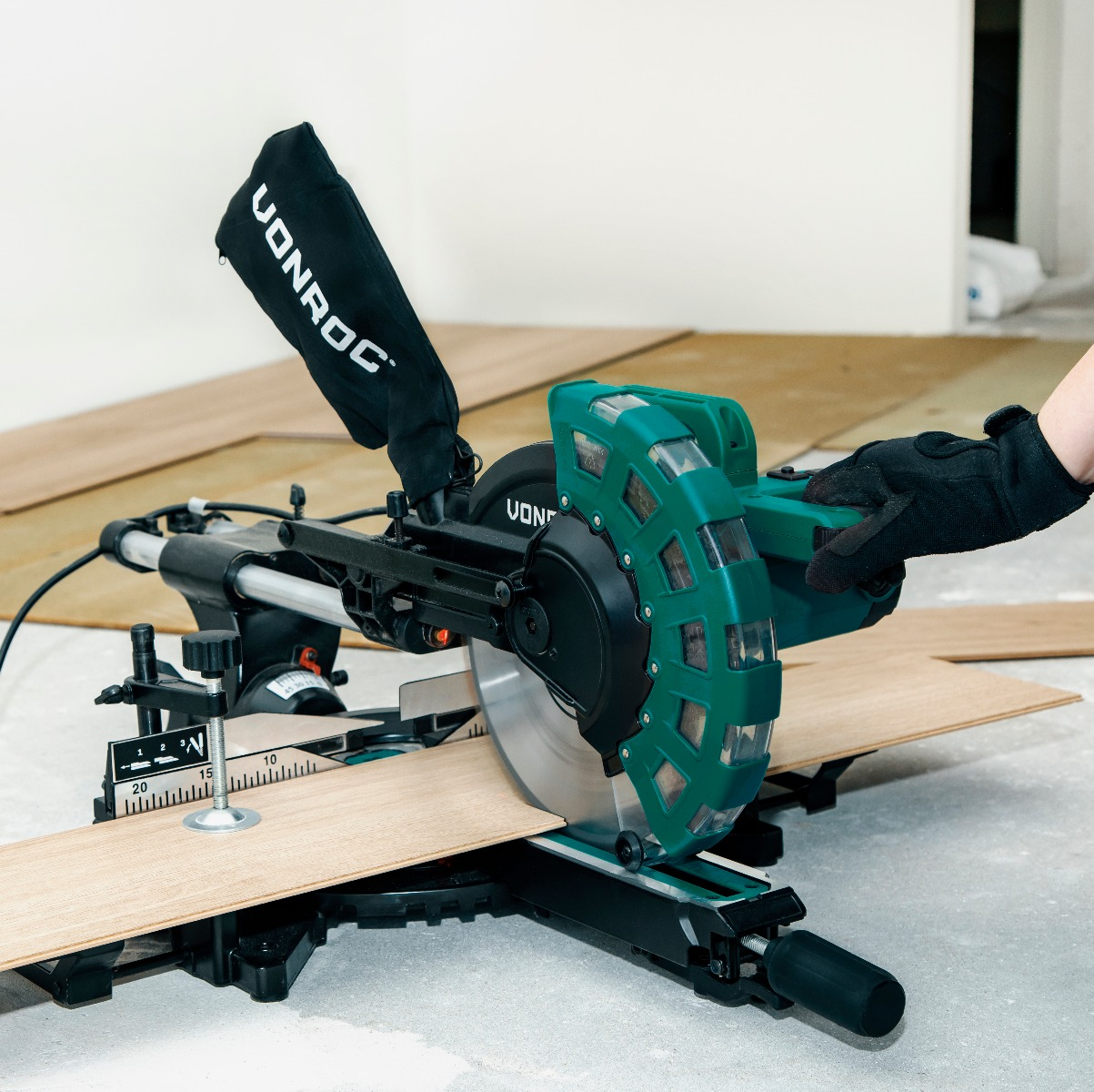 Een persoon gebruikt een cirkelzaag om een houten plank te zagen. De zaag is groen en zwart, met een stofzak en een zaagblad.