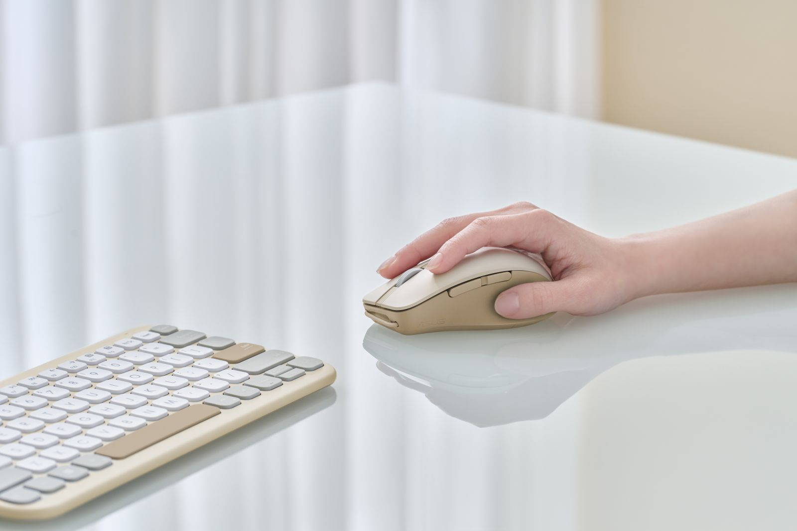 Een hand rust op een beige muis. Een toetsenbord staat op de voorgrond. De achtergrond is een wit, glanzend oppervlak.