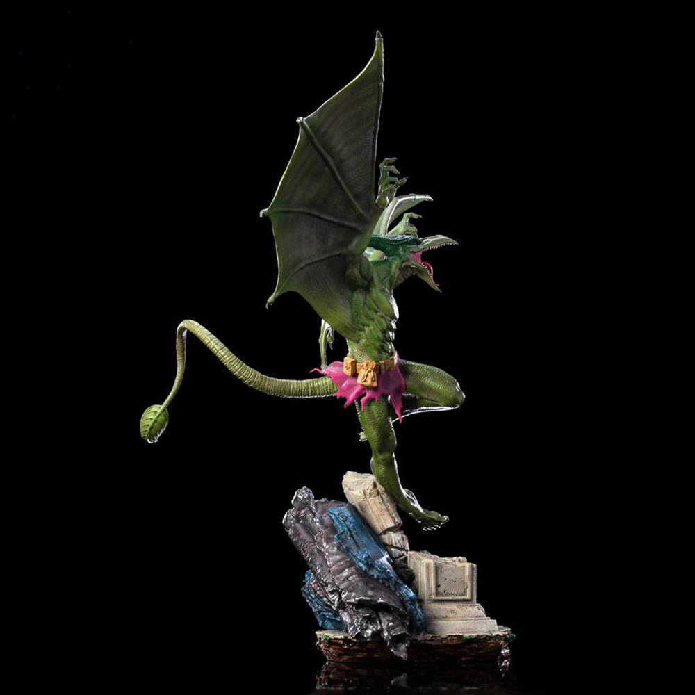Una creatura verde simile a un drago con ali e coda è in piedi su una roccia. Ha una gonna rosa e un'espressione minacciosa.