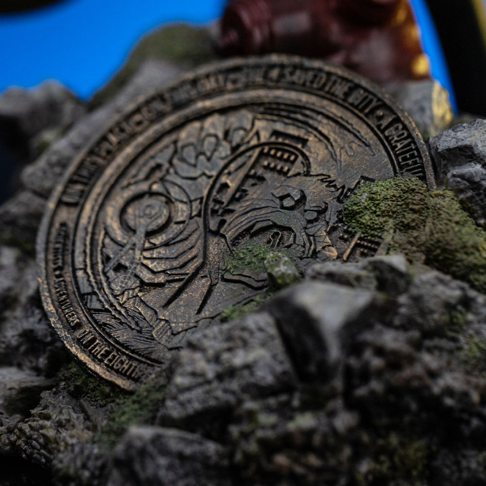 Una moneta di bronzo giace su rocce con muschio. La moneta ha incisioni e testo. Lo sfondo è sfocato con cielo blu.