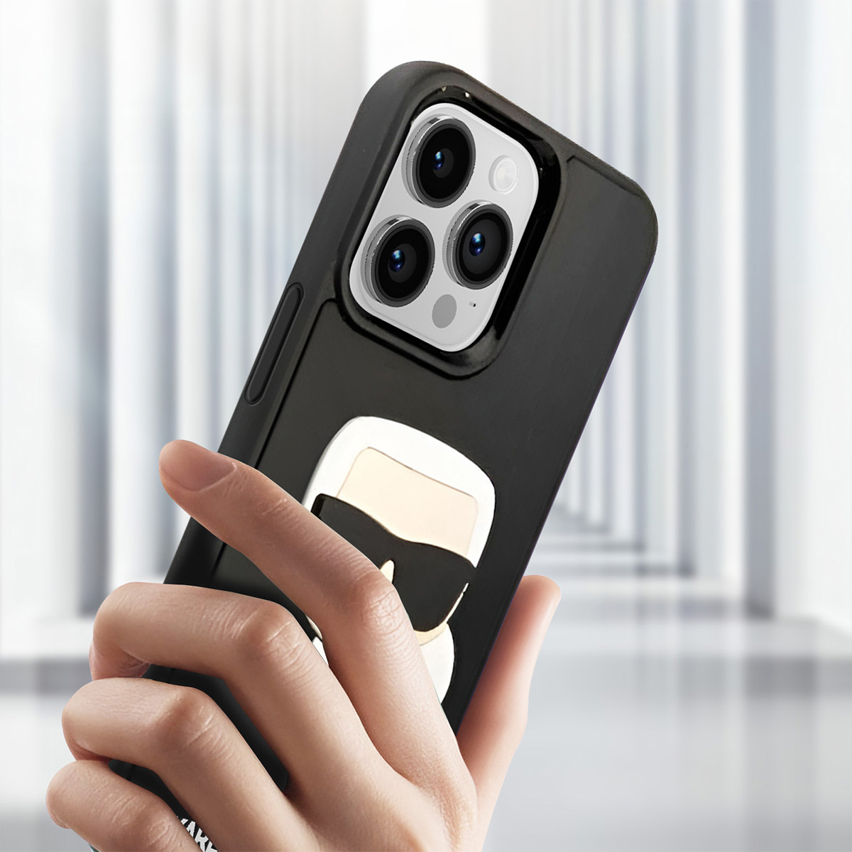 Mano che tiene un iPhone nero con una custodia Karl Lagerfeld. La custodia ha un logo di una persona con occhiali da sole.