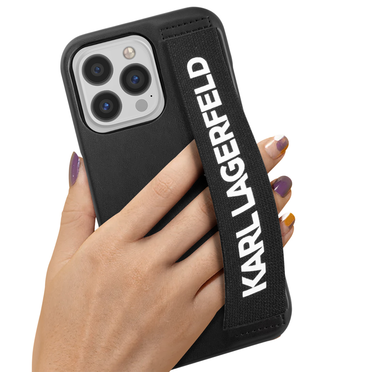 Eine Hand hält ein schwarzes Telefon mit einem Karl Lagerfeld-Riemen. Das Telefon hat eine Dreifach-Kamera. Die Nägel sind bunt lackiert.