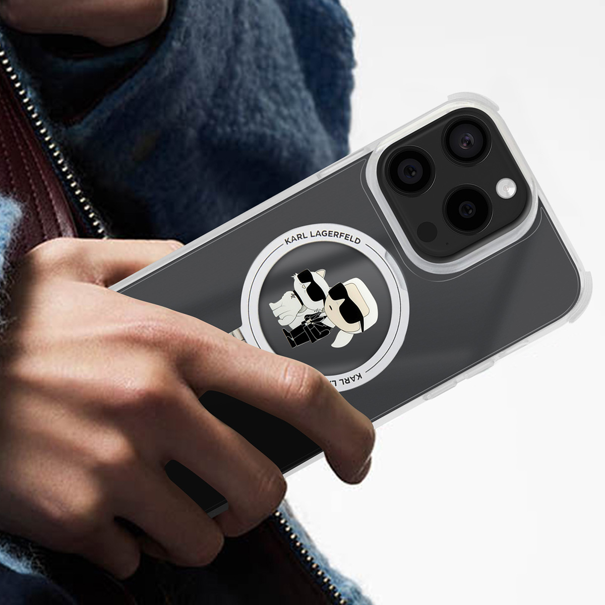Una persona tiene in mano un telefono con una custodia di Karl Lagerfeld. La custodia ha un logo con due personaggi dei cartoni animati con occhiali da sole. Il telefono ha delle fotocamere.