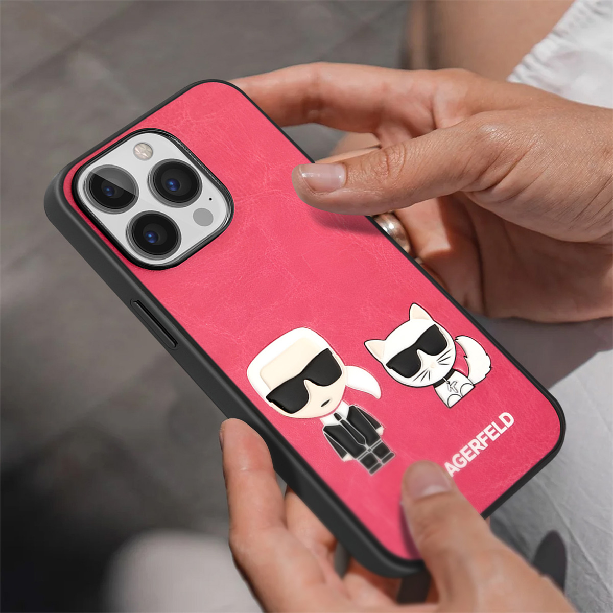 Una mano tiene una custodia rossa per telefono con Karl Lagerfeld e un design a cartoni animati di gatti. Il telefono ha una cornice nera.