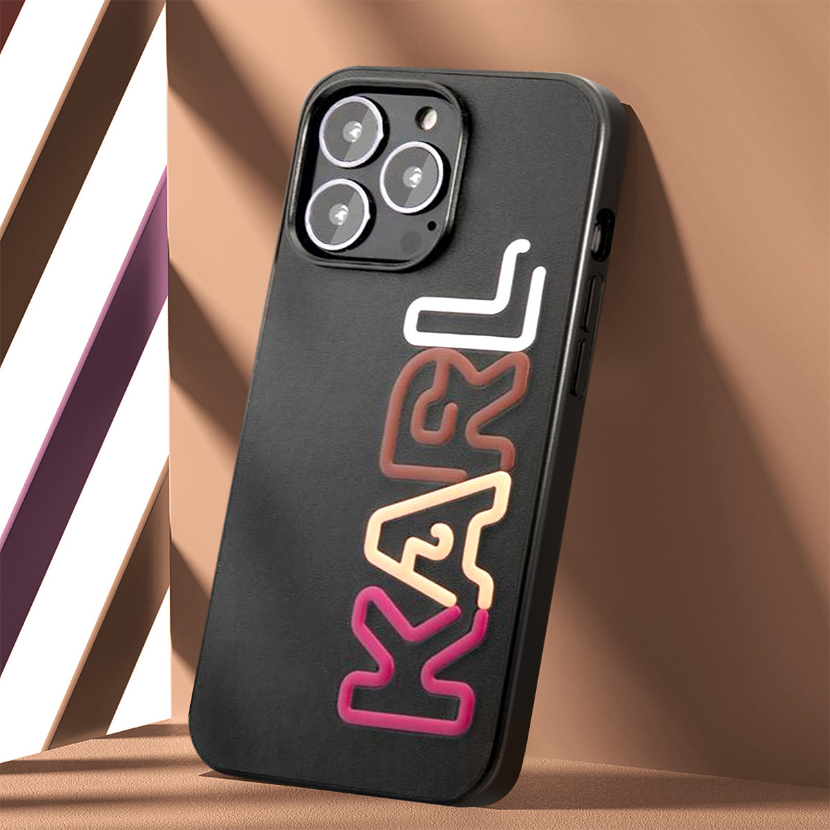 Una custodia nera con la scritta KARL in bianco, marrone, rosa e beige. Il telefono ha tre lenti della fotocamera.